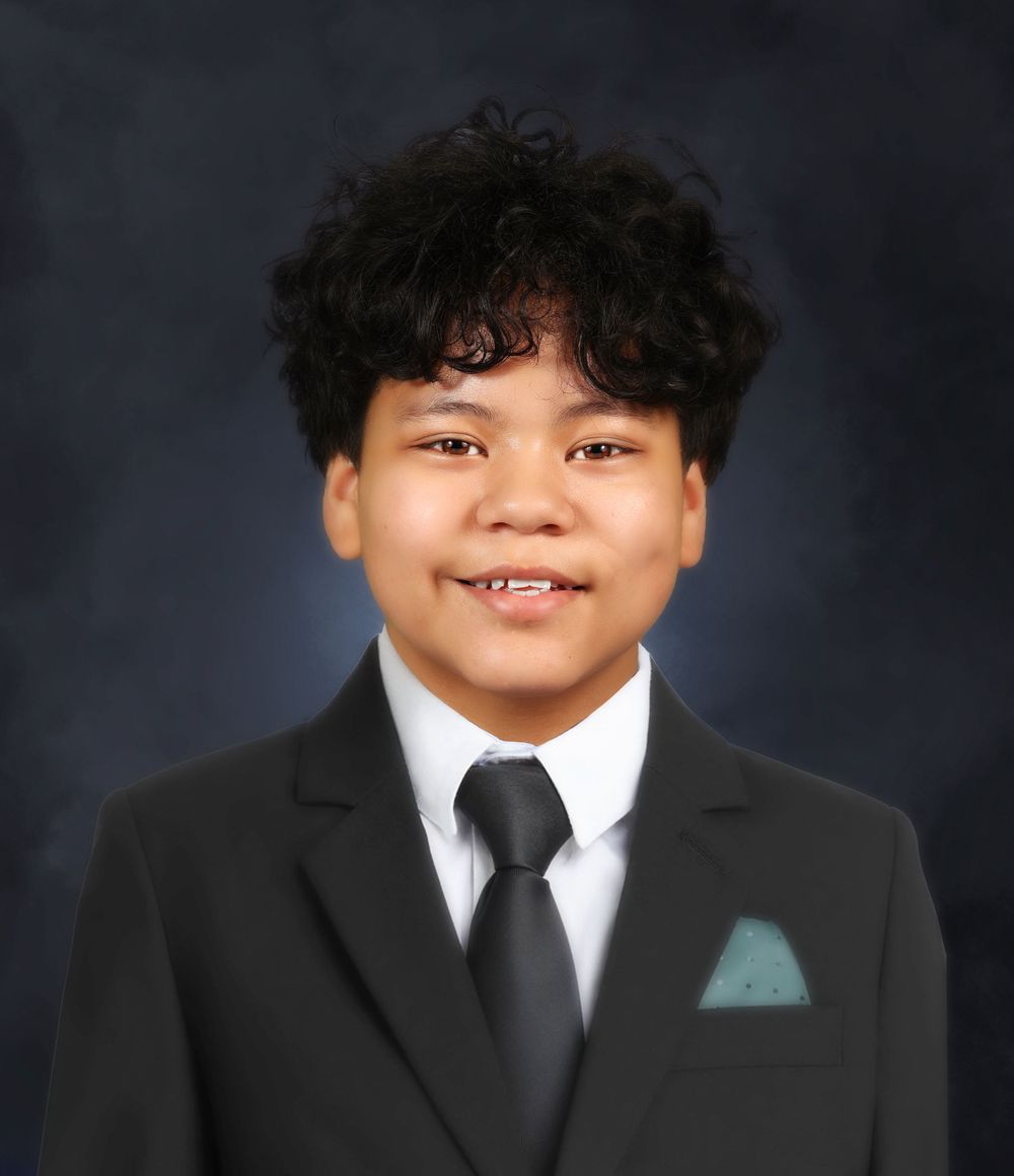 Professional headshot in black suit with teal pocket square against dark background.