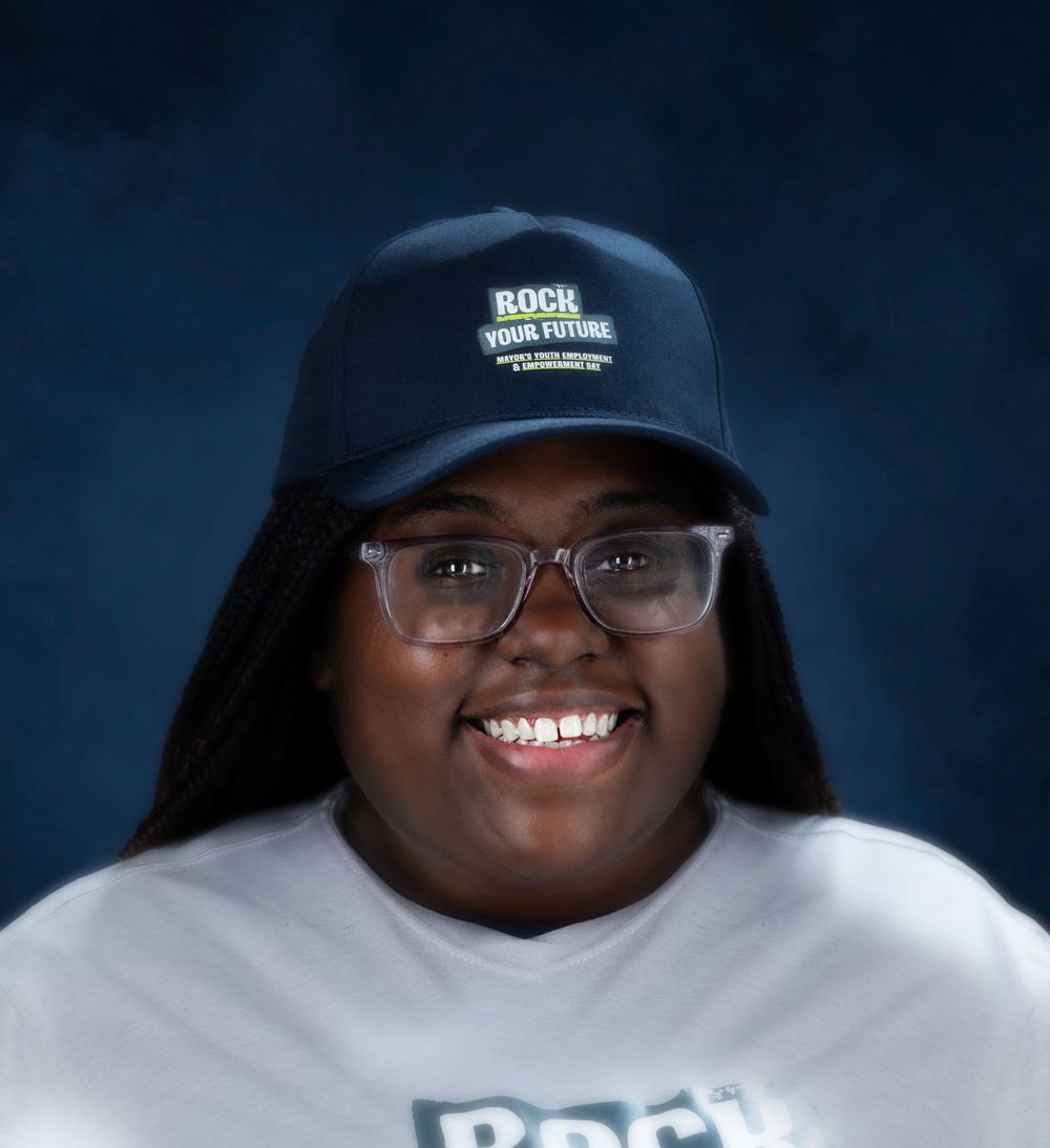 Studio portrait wearing baseball cap, glasses and white sweatshirt against blue background.