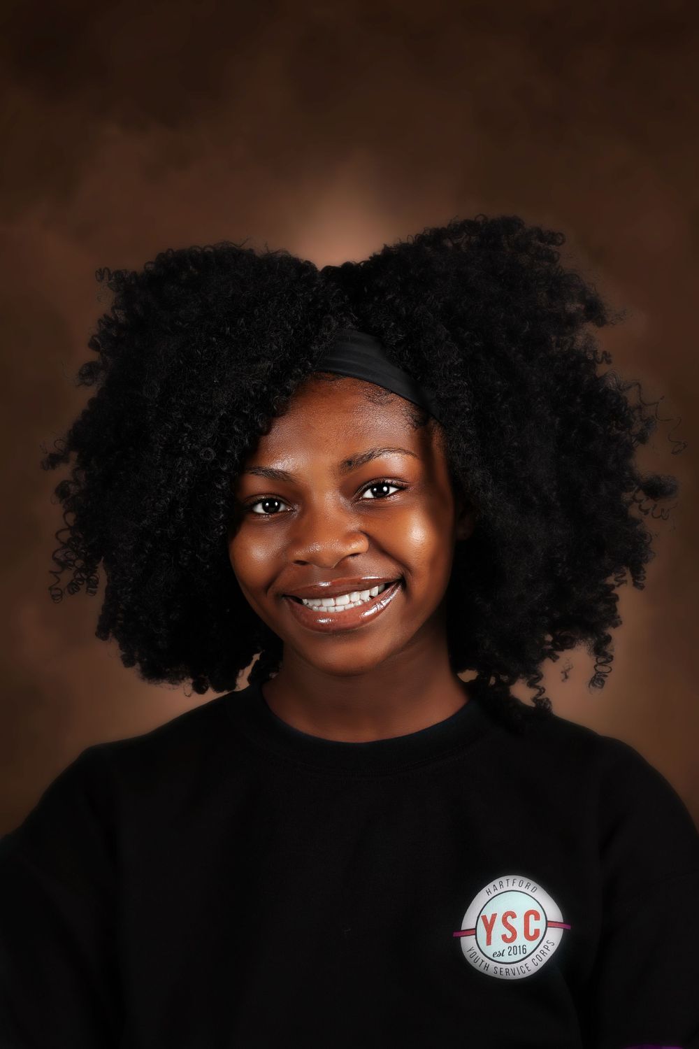 Studio portrait showcasing natural afro hairstyle and bright smile against brown background.