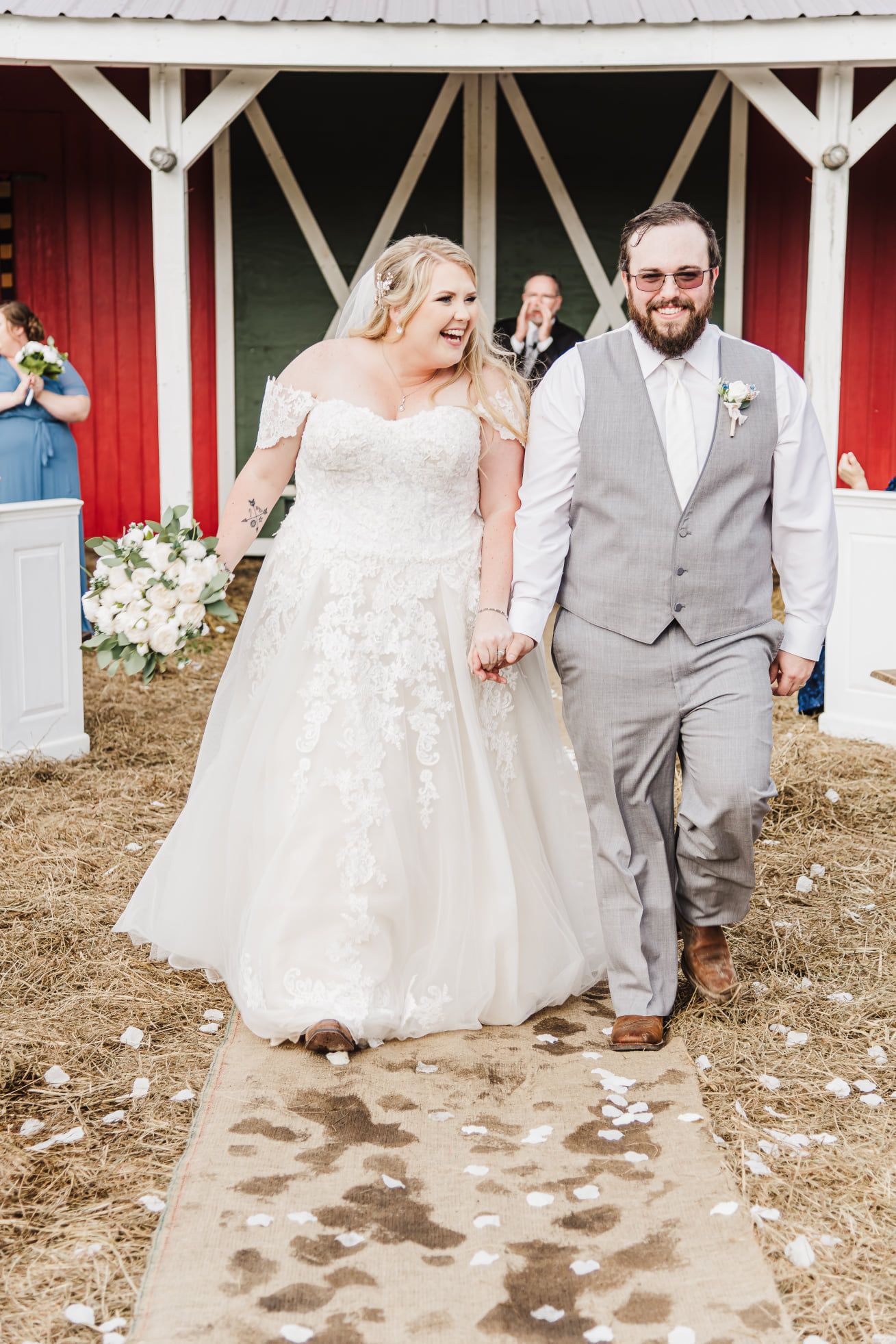 A joyful wedding couple exits their ceremony in front of a red barn.
