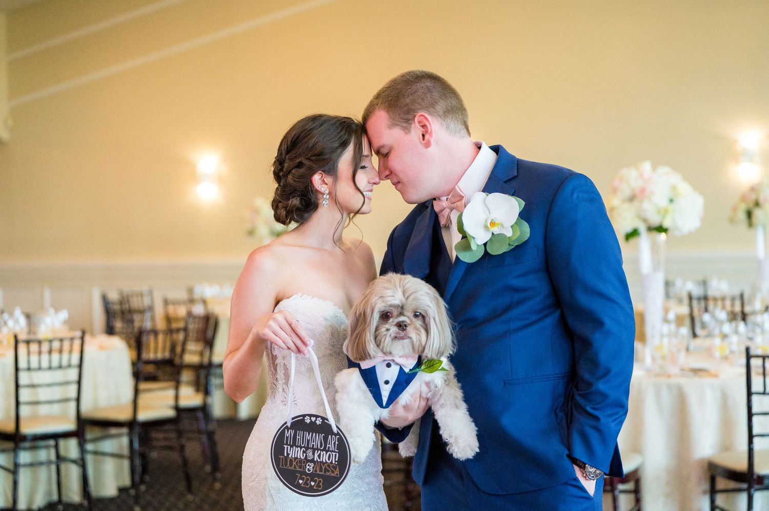 Couple standing face-to-face holding their dog who looks on, on their wedding day.