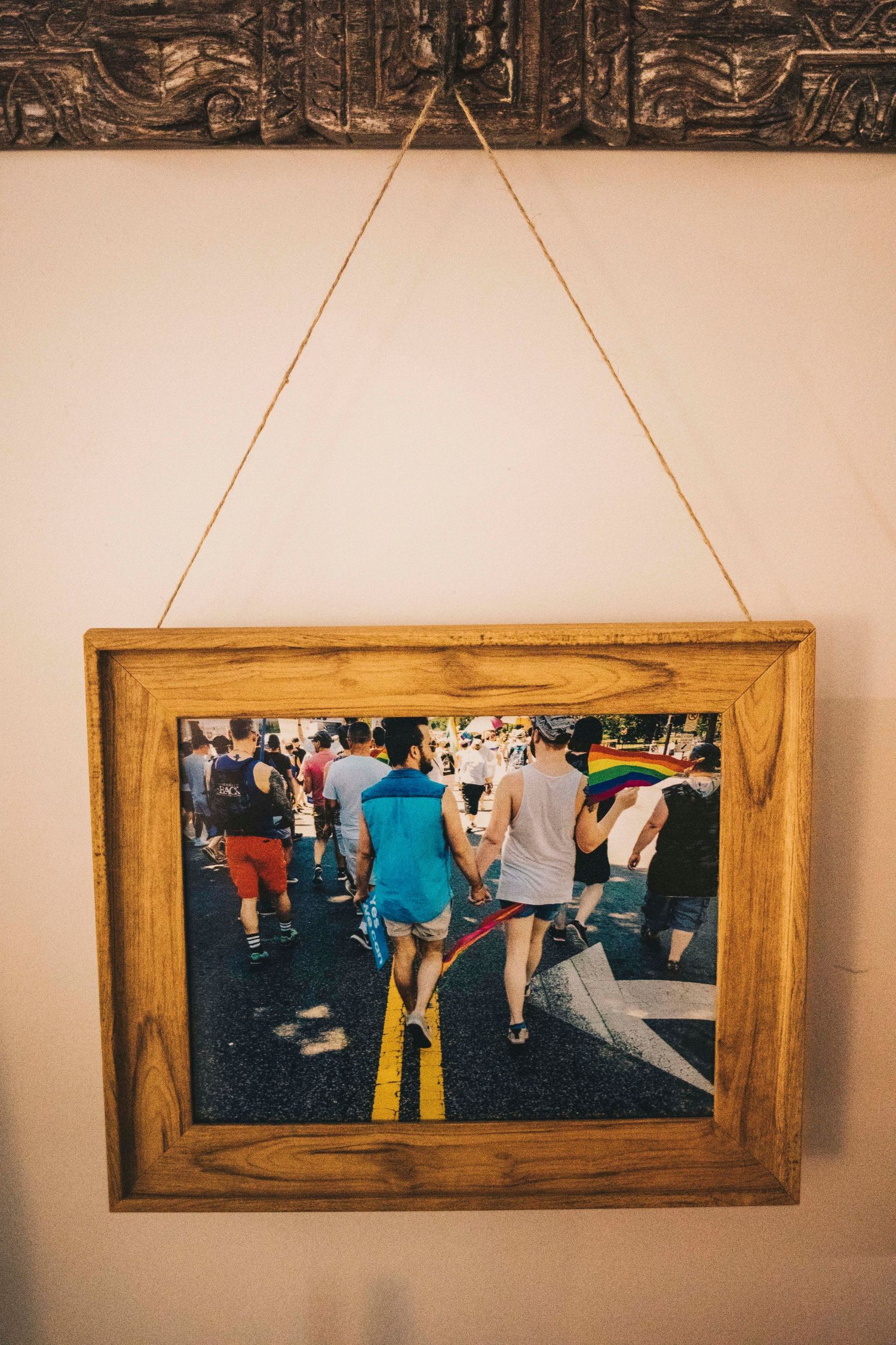 Wooden framed photo of couple holding hands at Pride parade hanging on wall with rope.
