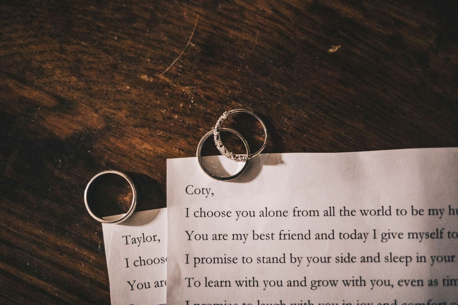 Two gold wedding bands resting on handwritten wedding vows addressed to Cory and Taylor.
