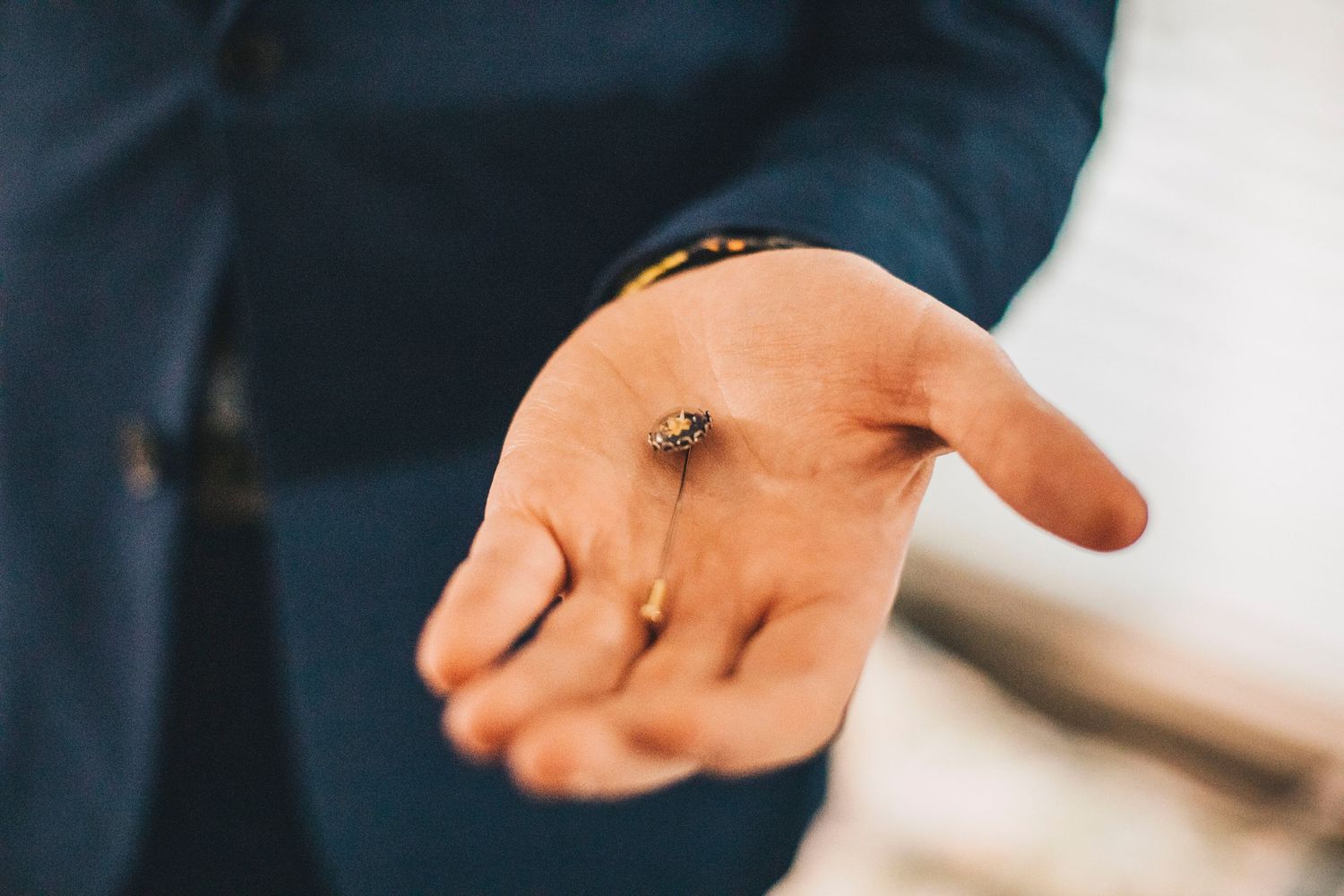 Groom in blue suit holding small floral boutonniere in outstretched palm before wedding ceremony.