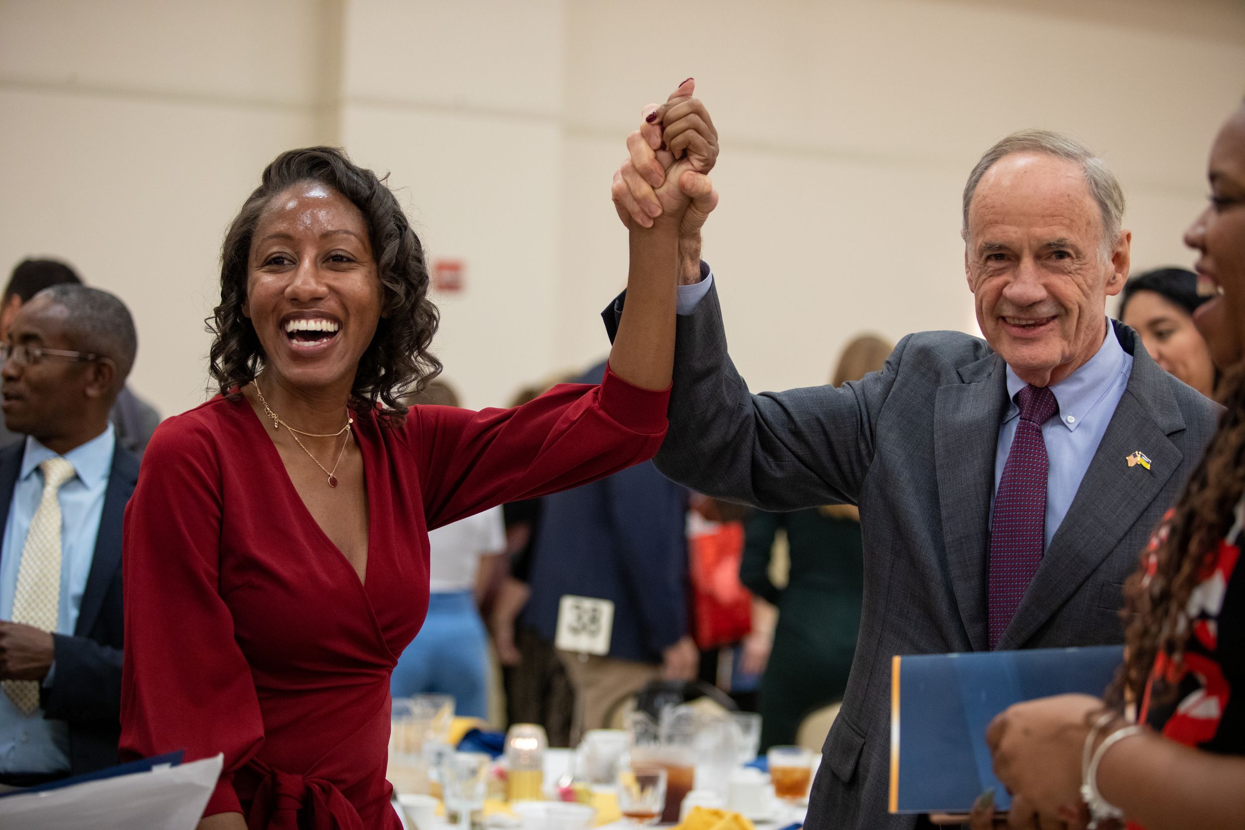 Two people raising joined hands in celebration during a formal indoor event.