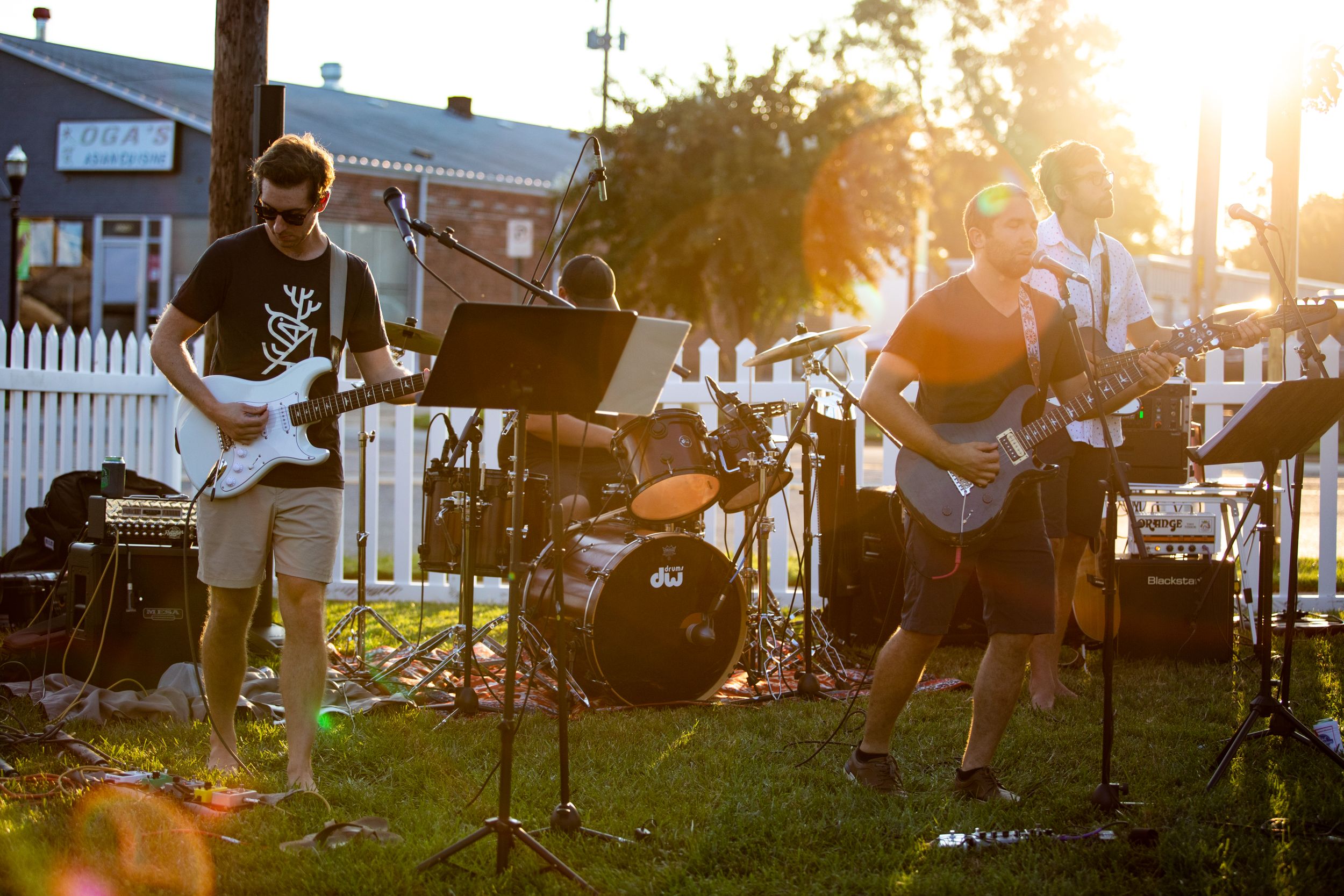 Musicians performing at sunset with guitars and drums on an outdoor stage.