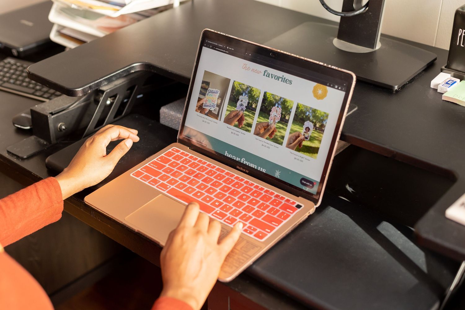 Person typing on a rose gold laptop displaying a photography website on a dark desk.