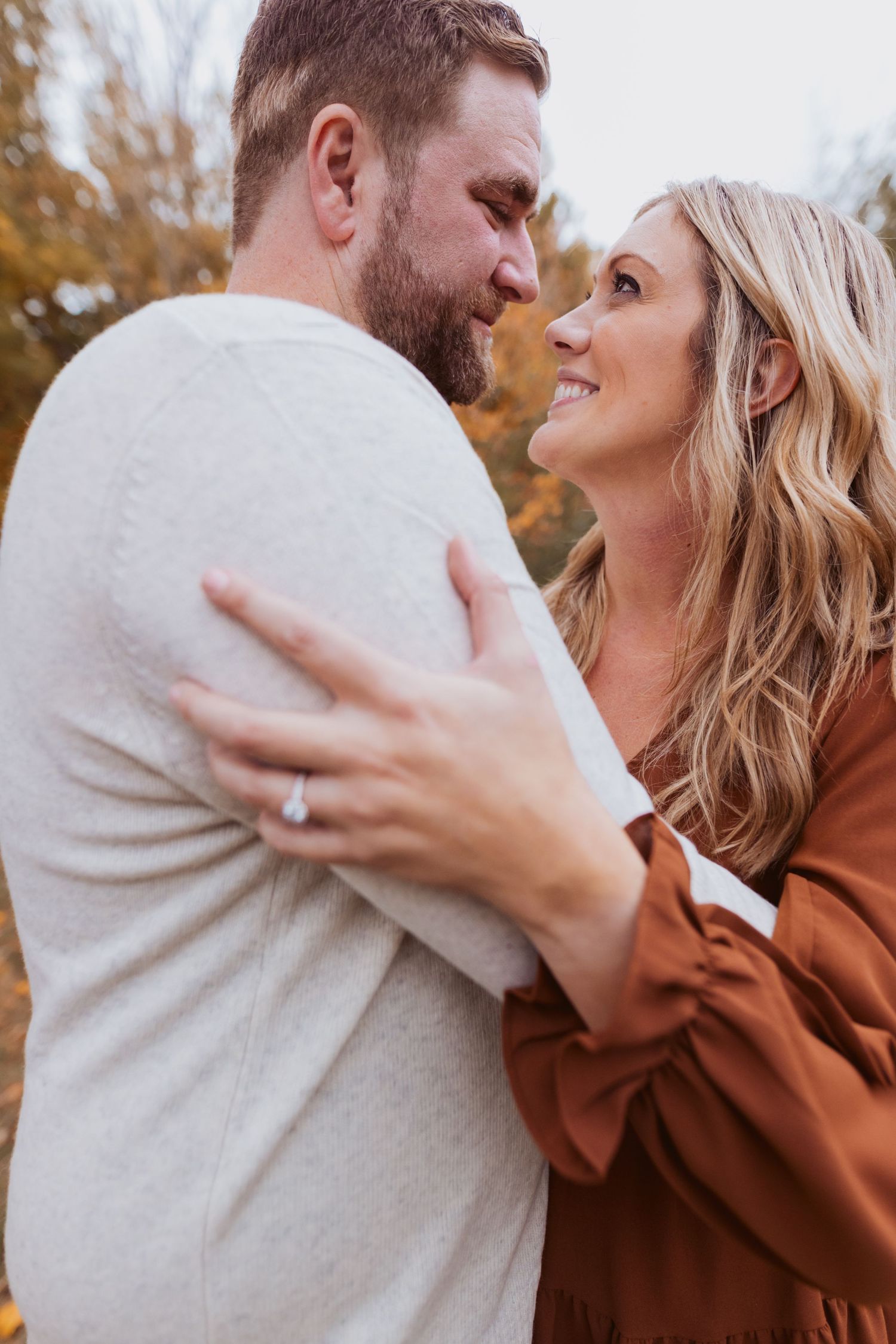 Romantic couple embraces in autumn setting wearing beige and brown clothing during intimate photoshoot.