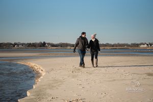 Two people walking together along a sandy beach shoreline with clear blue sky overhead.