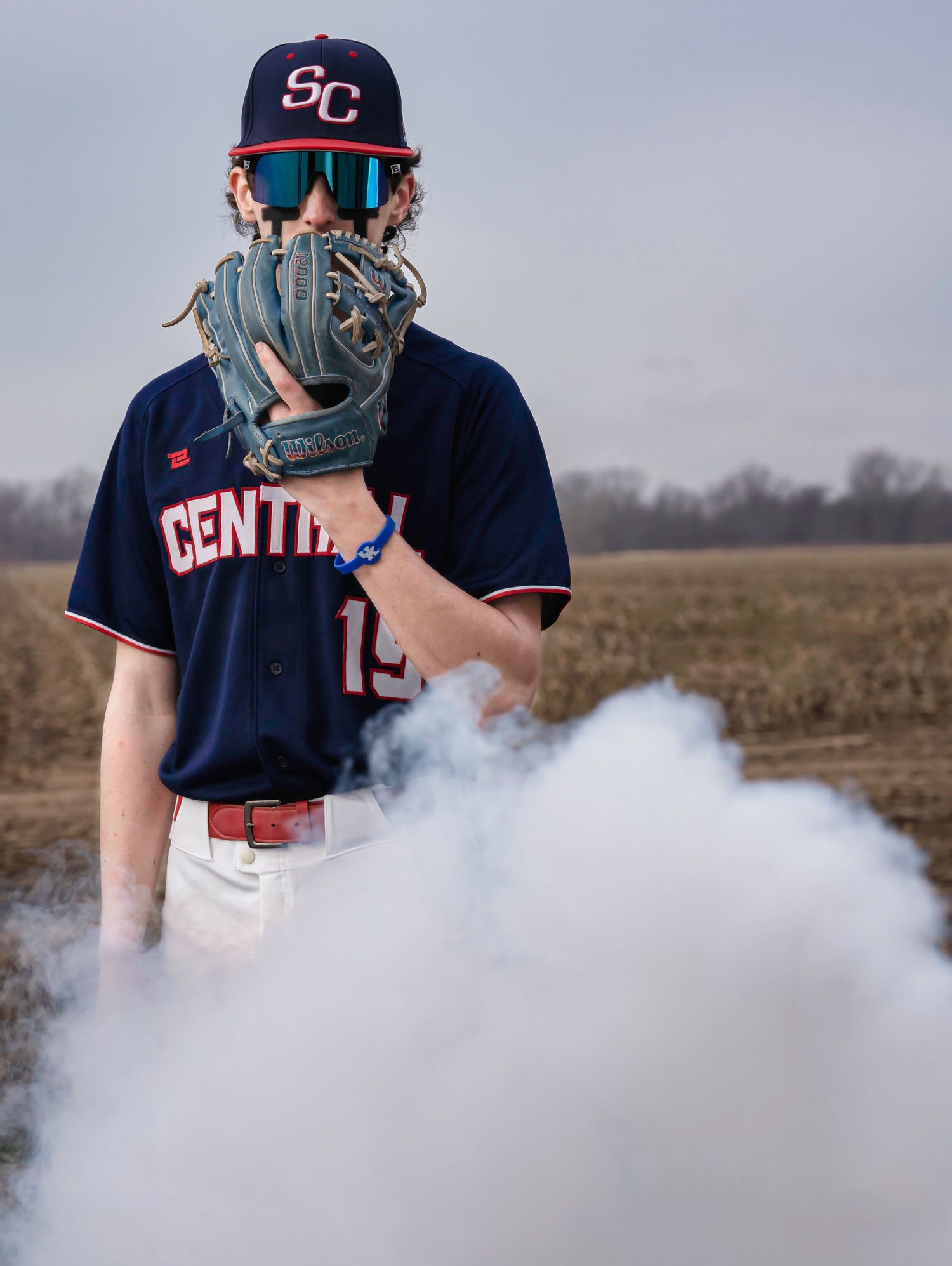 Baseball player in Central jersey with glove and sunglasses stands amid swirling smoke effect.