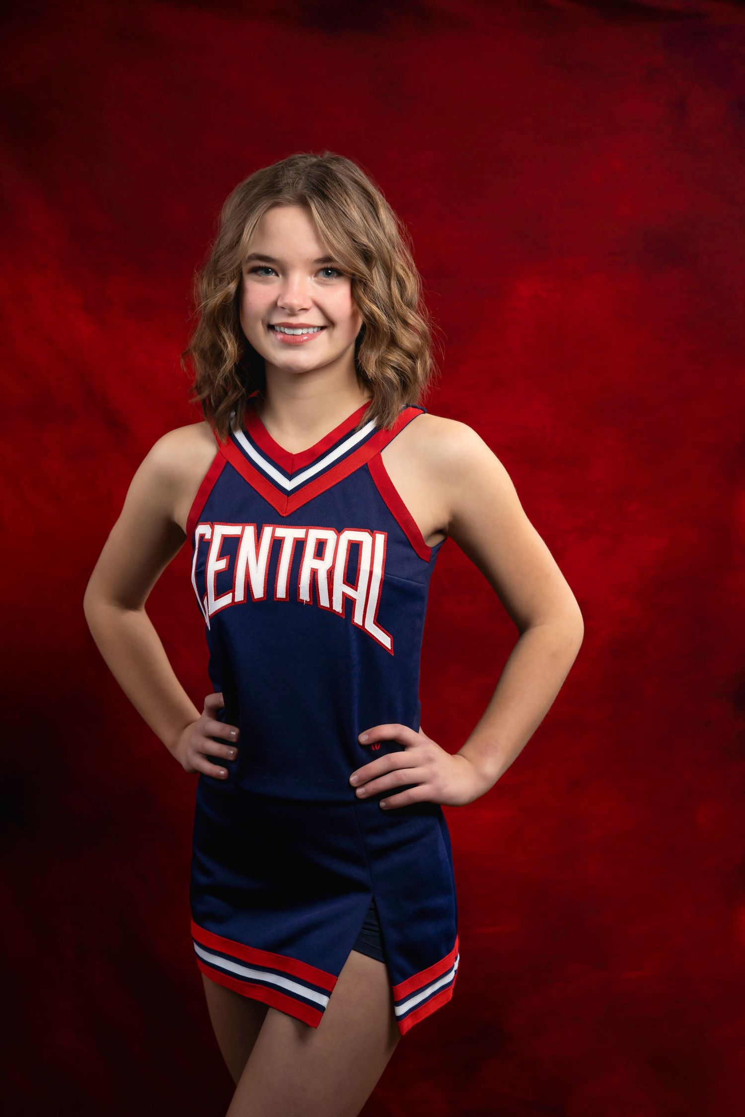Cheerleader poses in navy blue Central uniform against red backdrop.
