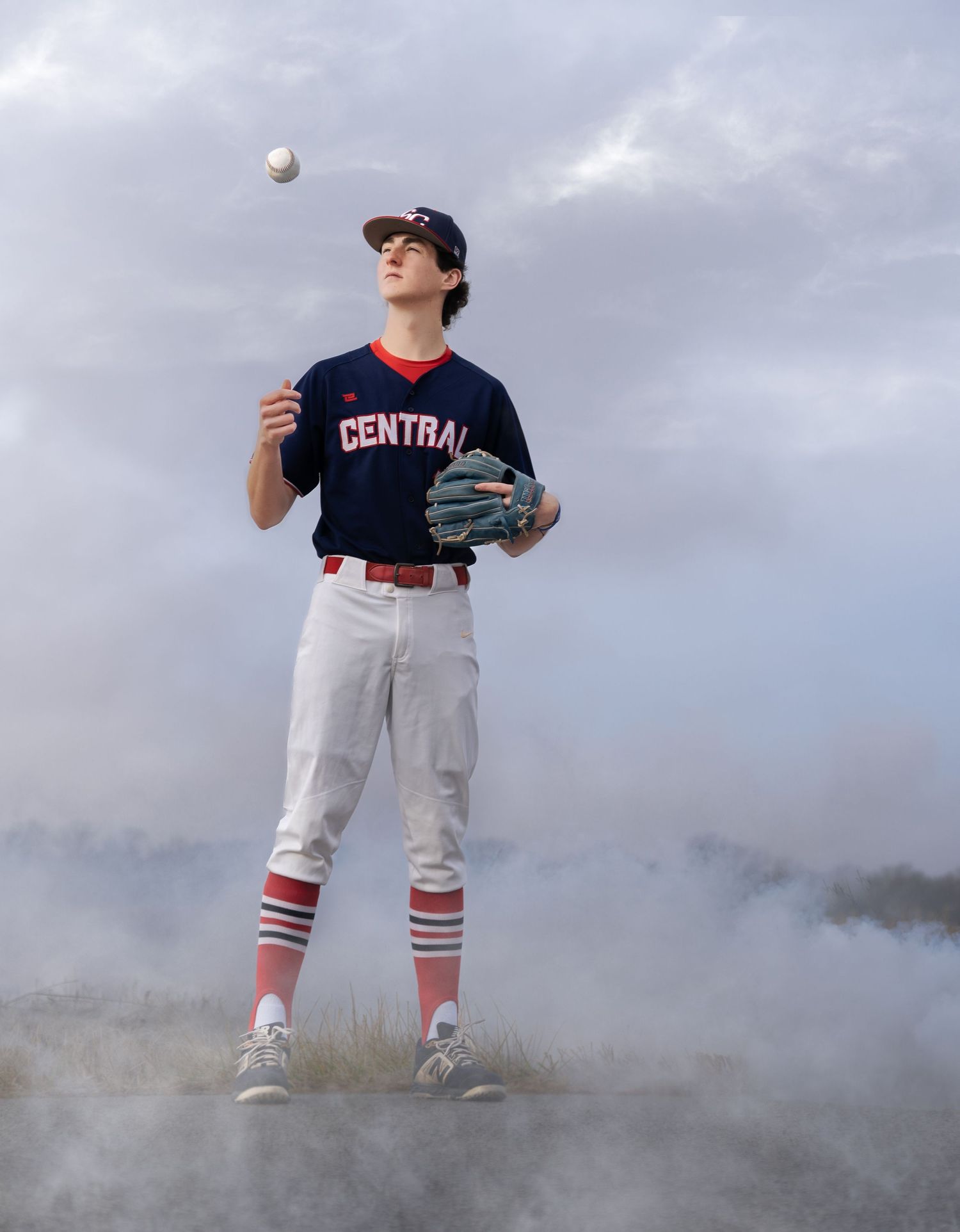 Baseball player in Central uniform tosses ball against cloudy sky with dramatic fog effect.