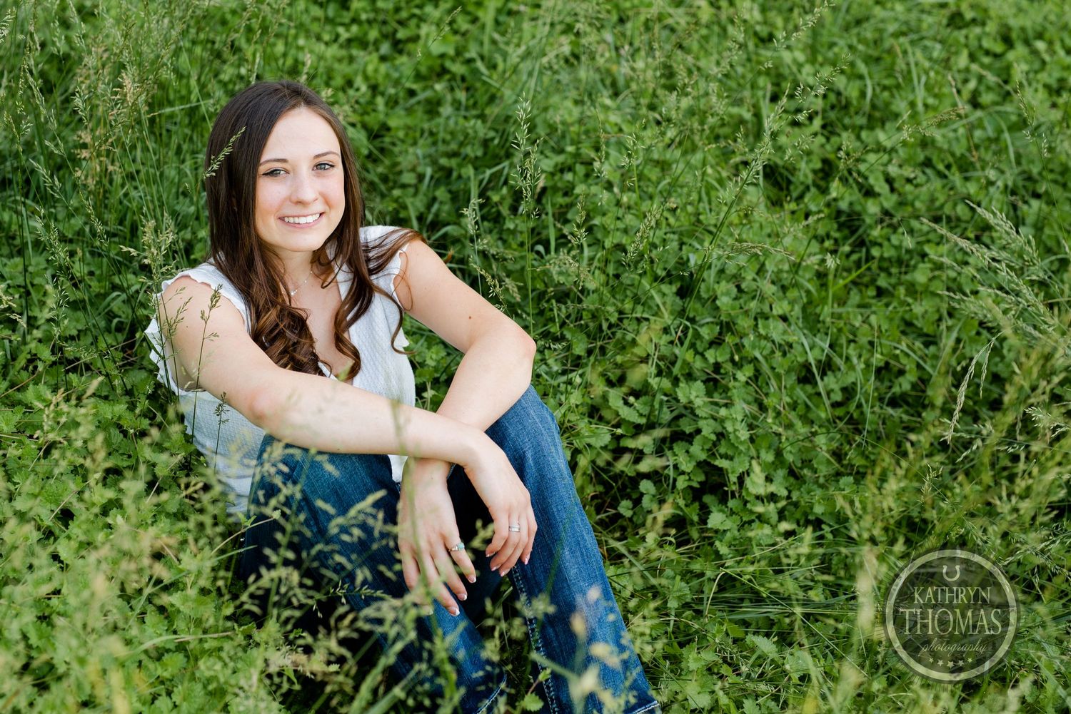A casual outdoor portrait amidst lush green vegetation wearing blue jeans.