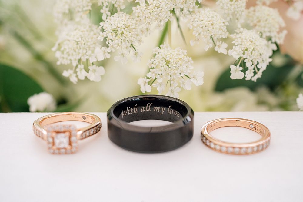 Three wedding rings displayed on white surface with delicate white flowers in background.