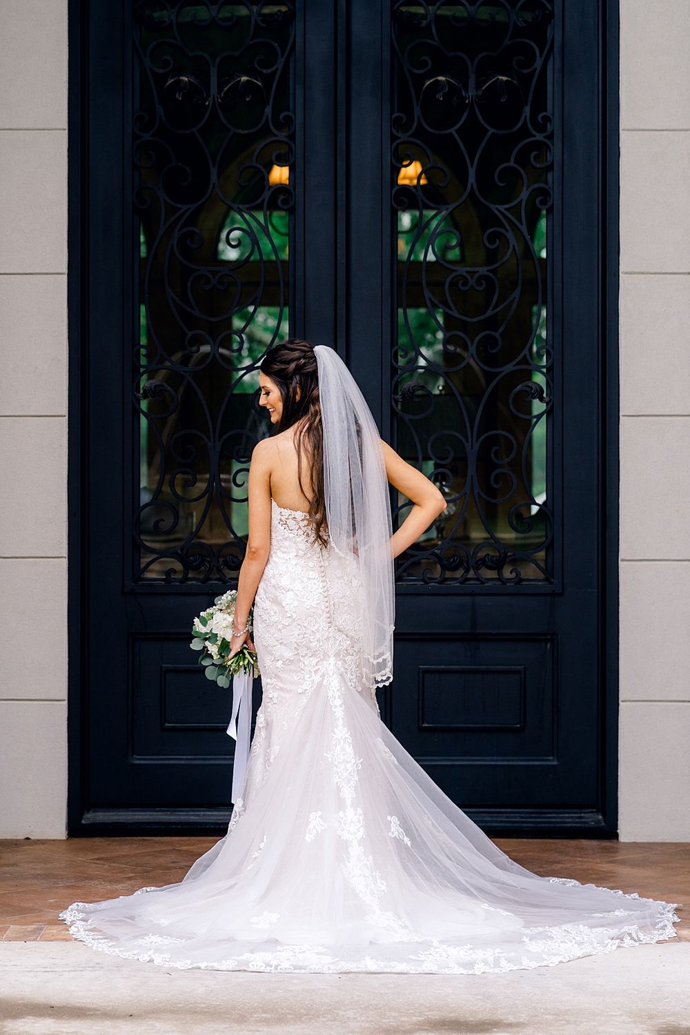 Classic bridal portrait featuring a flowing veil and fitted lace gown against ornate doors.