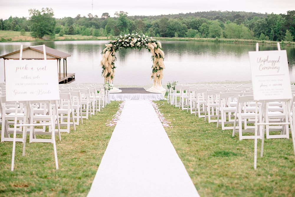 Lakeside wedding ceremony setup with white chairs and a floral arch at the altar.