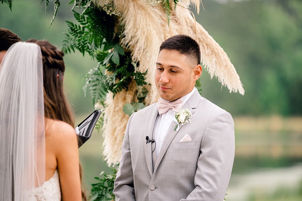 Intimate wedding ceremony moment under an arch decorated with pampas grass and greenery.