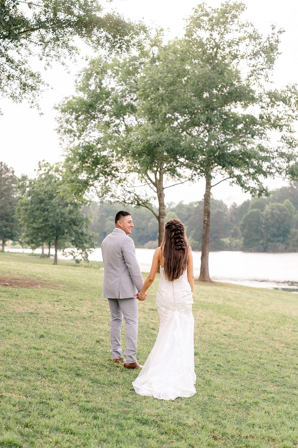 Scenic lakeside wedding portrait of couple holding hands while overlooking the water.