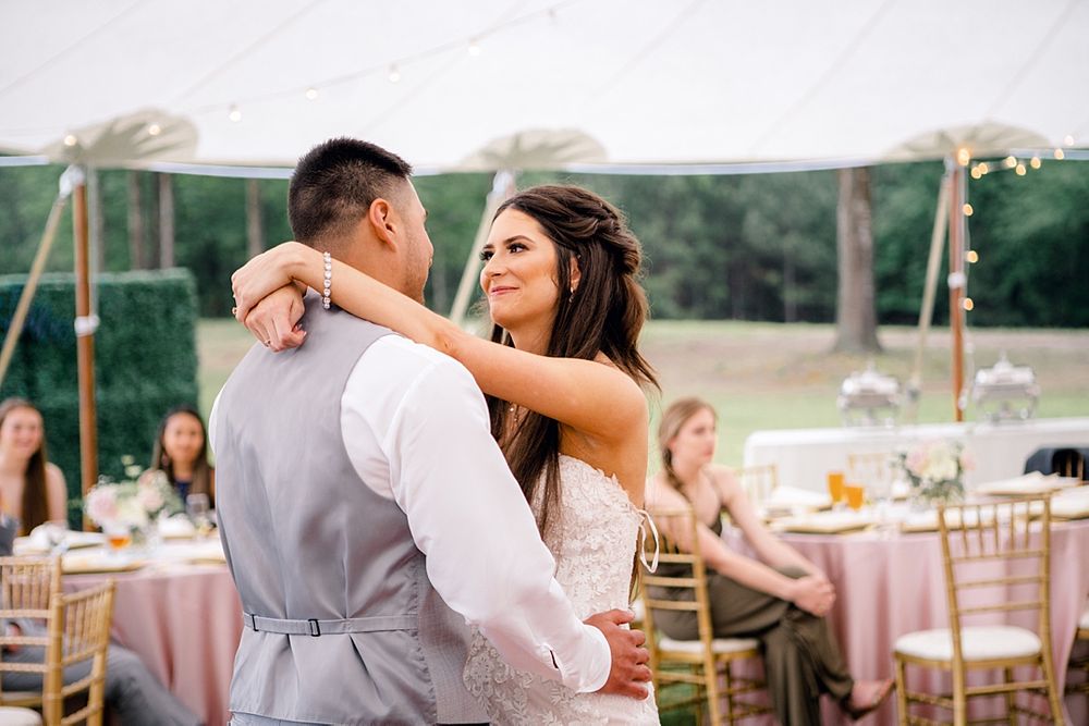 Reception first dance between newlyweds under white tent with table settings in background.