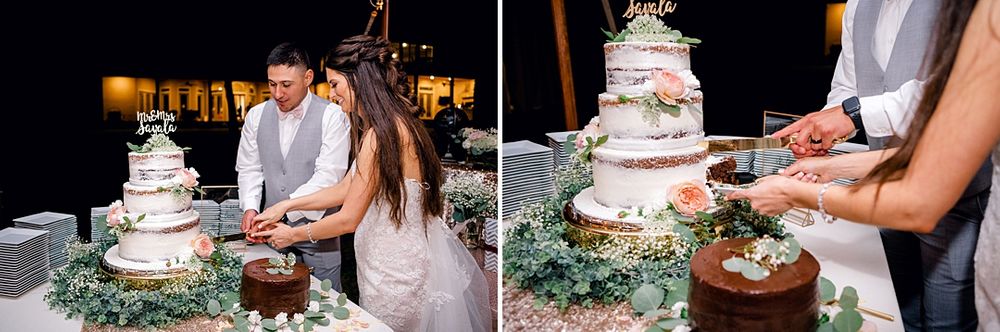 Newlyweds cutting their elegant white wedding cake decorated with greenery.