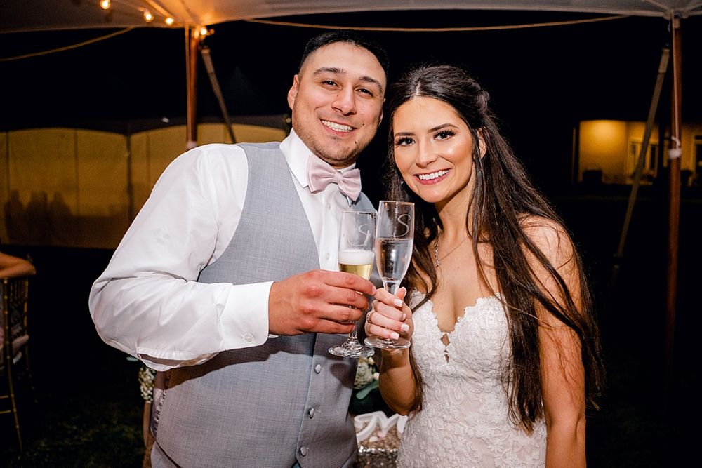 Newlyweds toast with champagne glasses during their evening reception celebration.