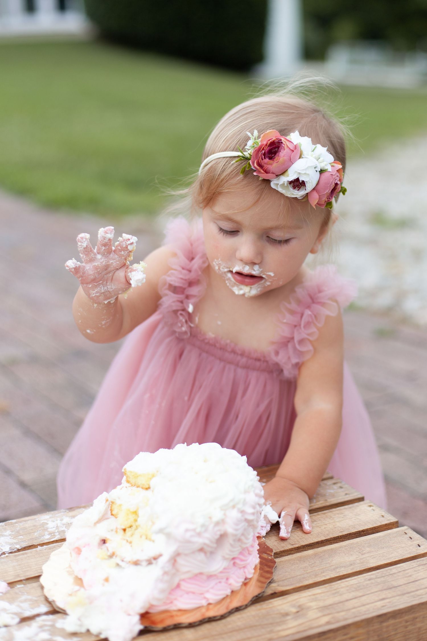 A one year old girl eats her cake in a pink dress at Historic Oak View Park in Raleigh, NC.