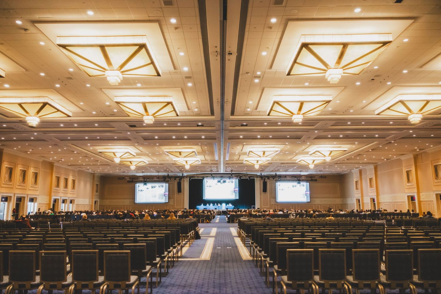 Large conference hall with rows of chairs and multiple screens set up for an event.