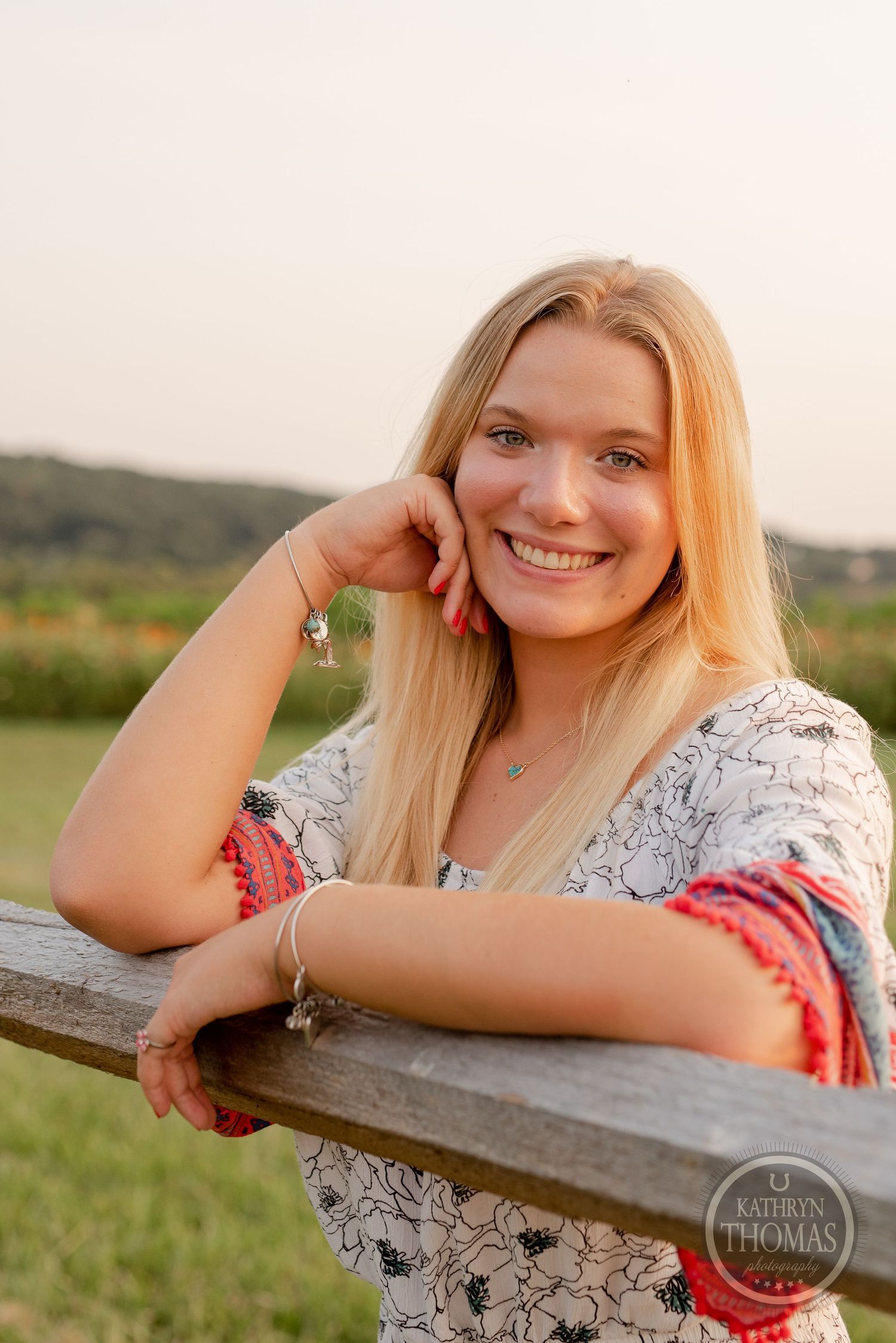 A woman leans on a wooden fence at sunset in a floral print top.