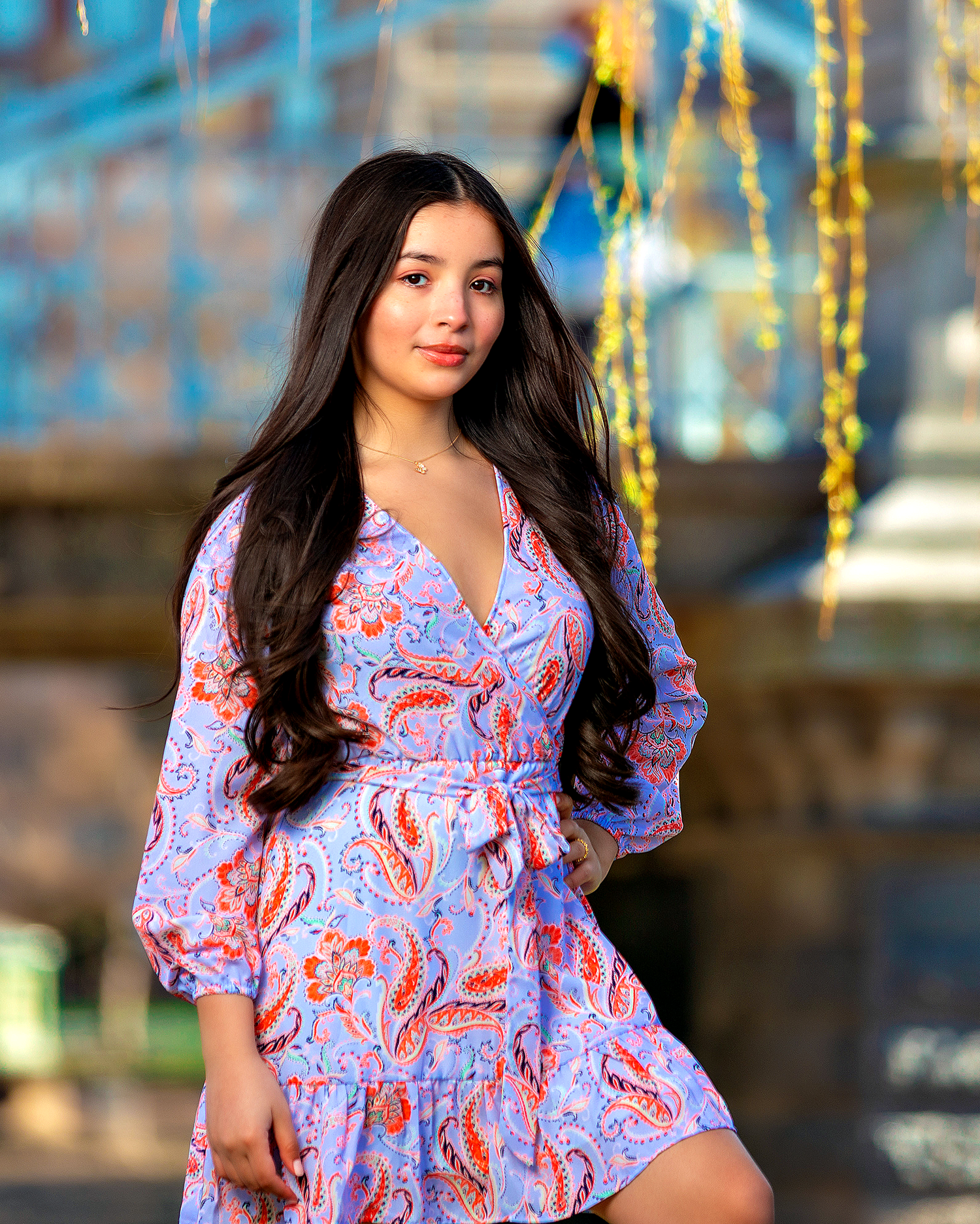 Outdoor fashion shoot in purple paisley wrap dress with balloon sleeves against golden decorations.
