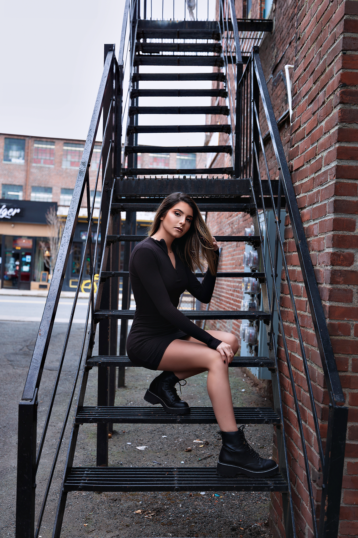 Urban fashion portrait on black metal fire escape stairs wearing fitted black dress.