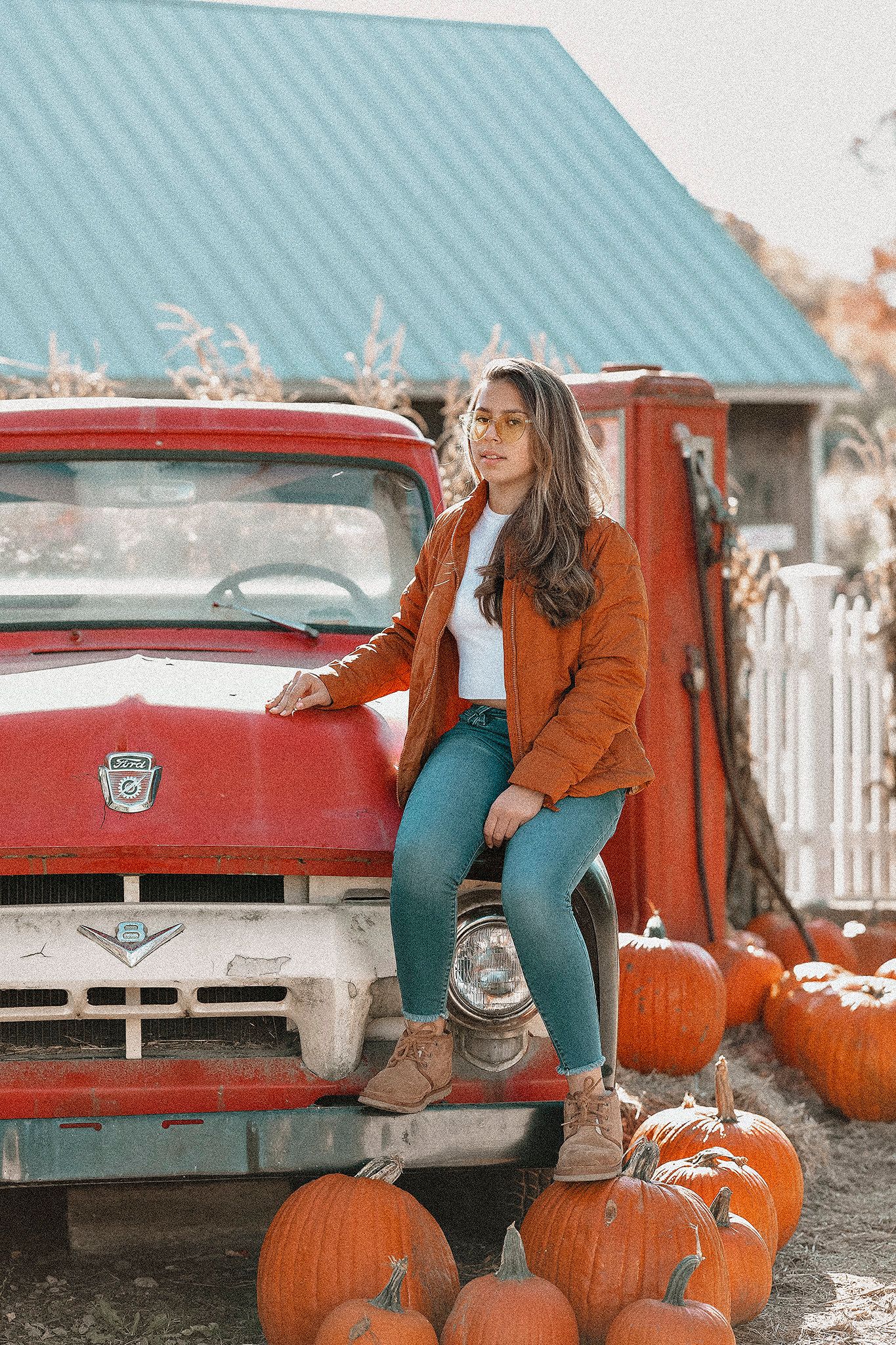 Vintage red pickup truck with pumpkins and rustic autumn farmhouse setting.
