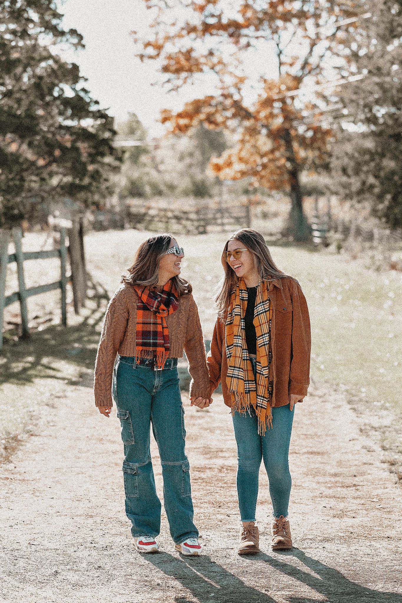 Two people in coordinated fall outfits walking together on a sunny country path.