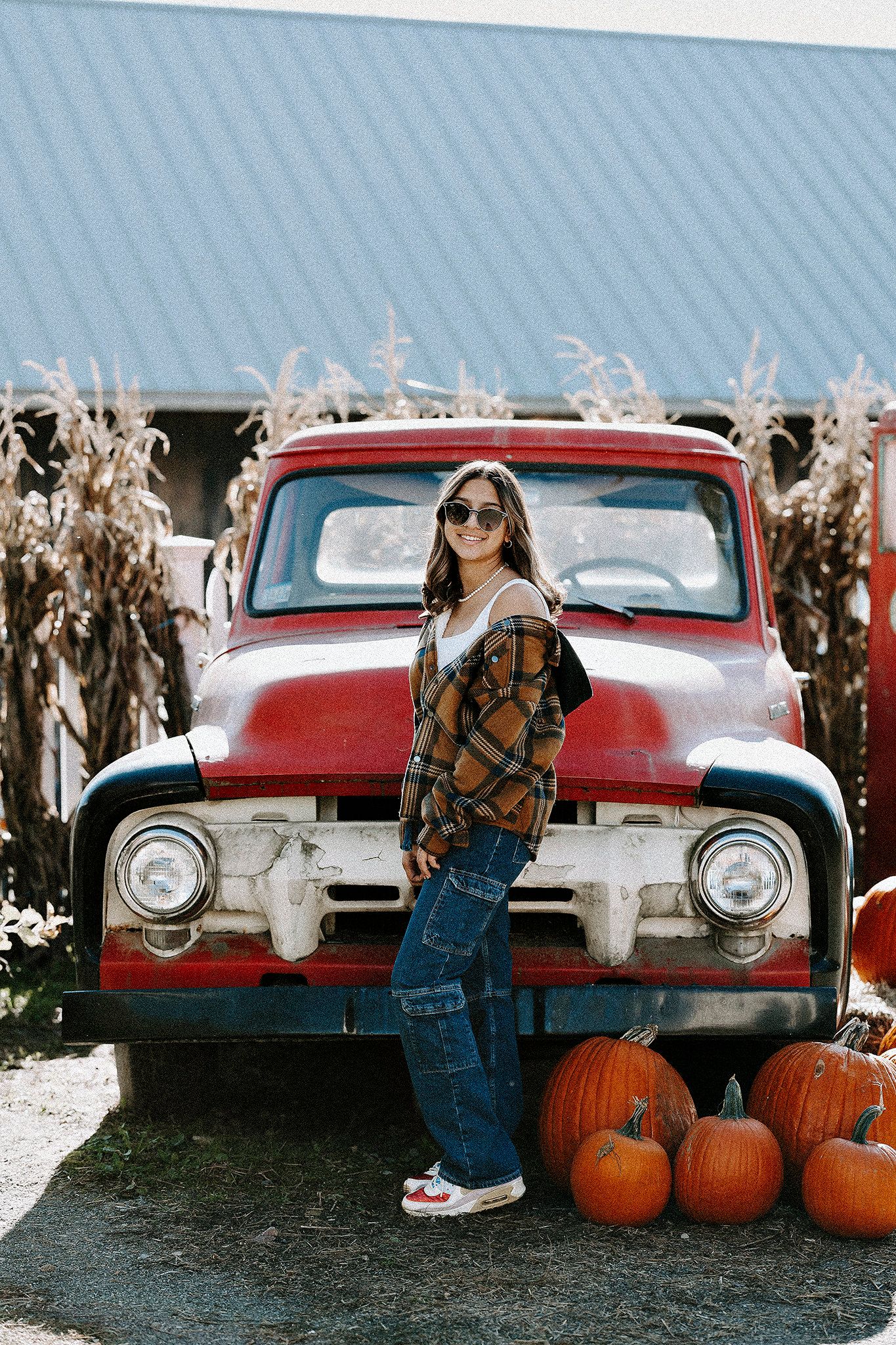 Classic red Ford truck with pumpkins and corn stalks in rustic fall setting.