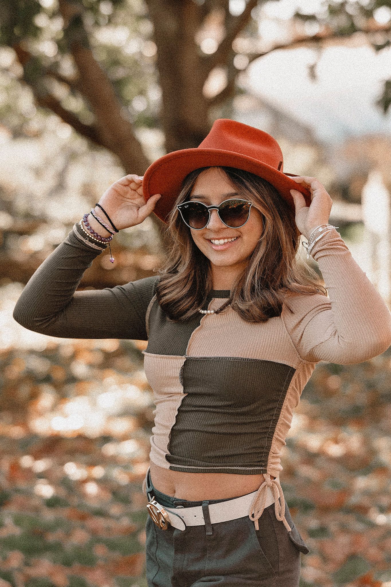 Autumn fashion with orange fedora and sunglasses against fall foliage background.