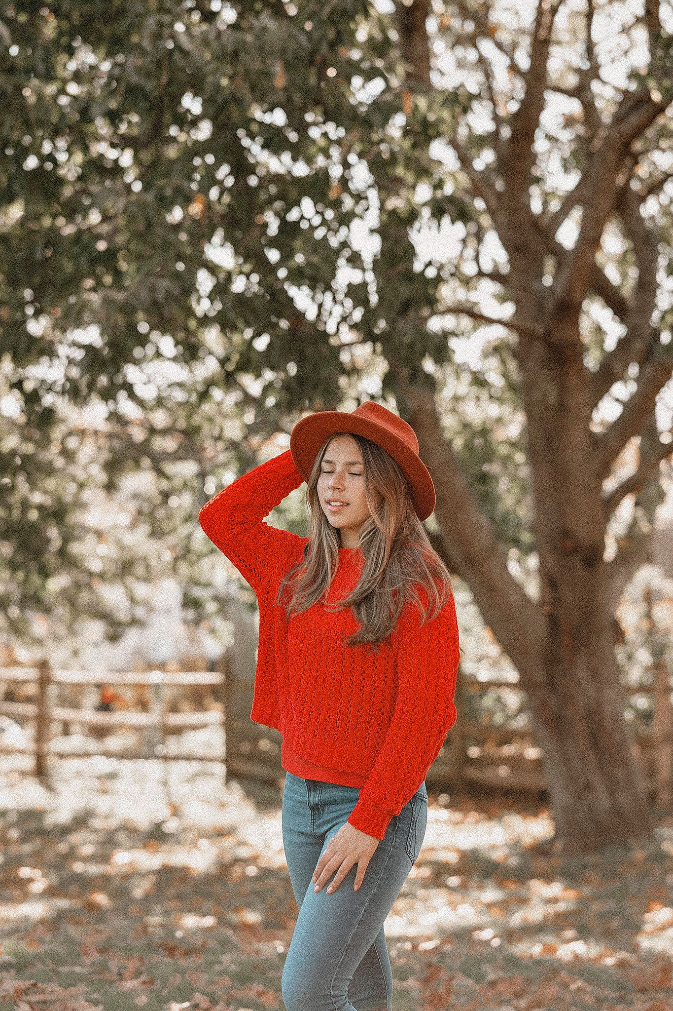 Casual fall outfit featuring bright red sweater and orange fedora in outdoor setting.