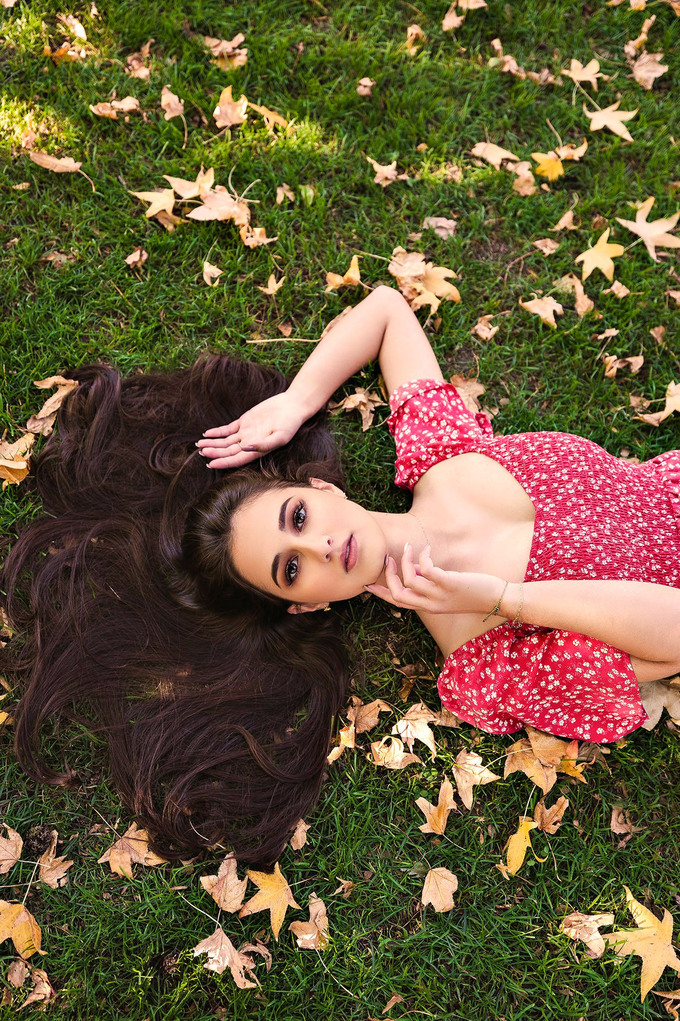 Overhead view of person in red polka dot dress lying on grass with autumn leaves.