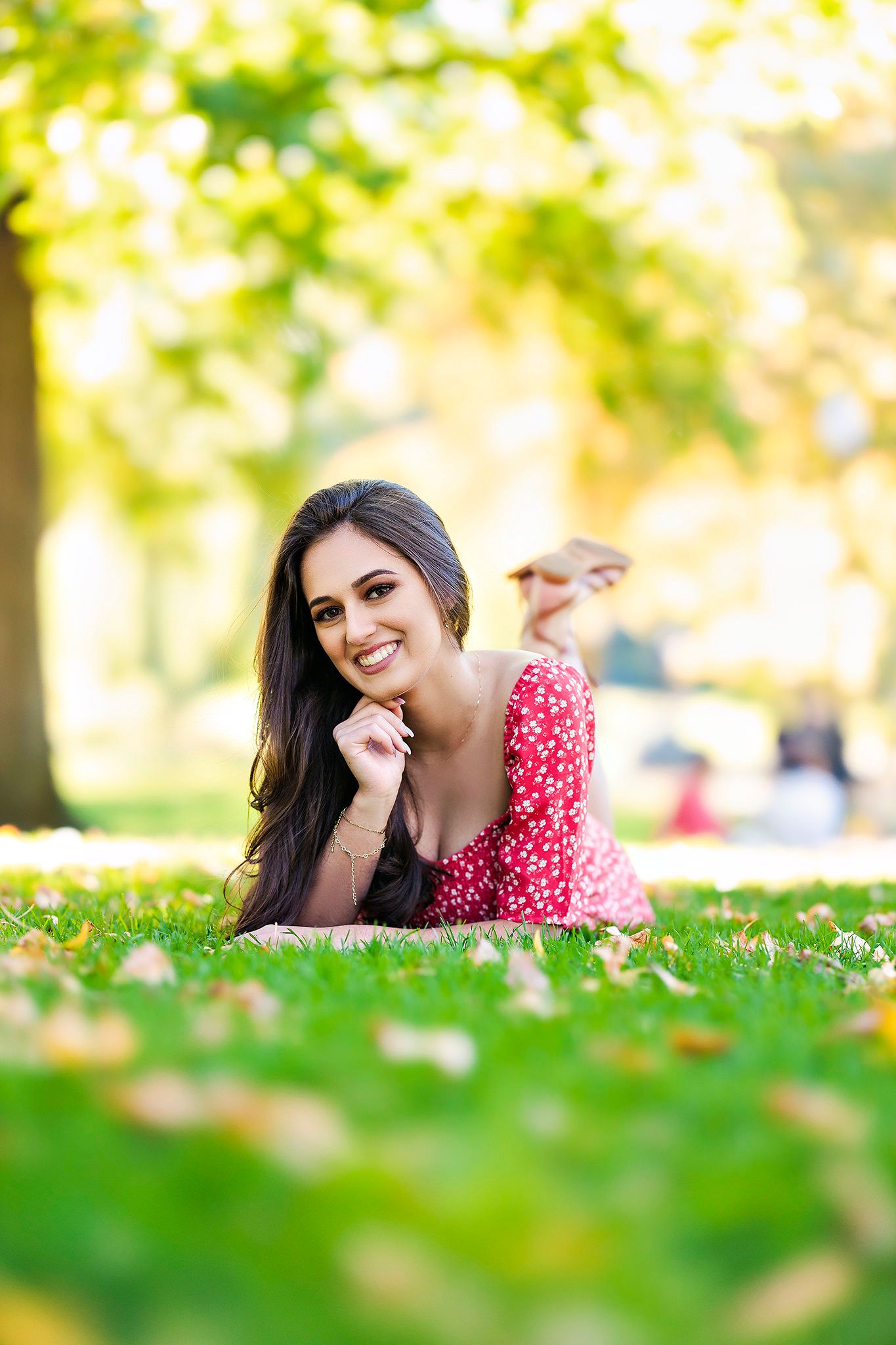 Outdoor autumn portrait lying on grass surrounded by fallen leaves.