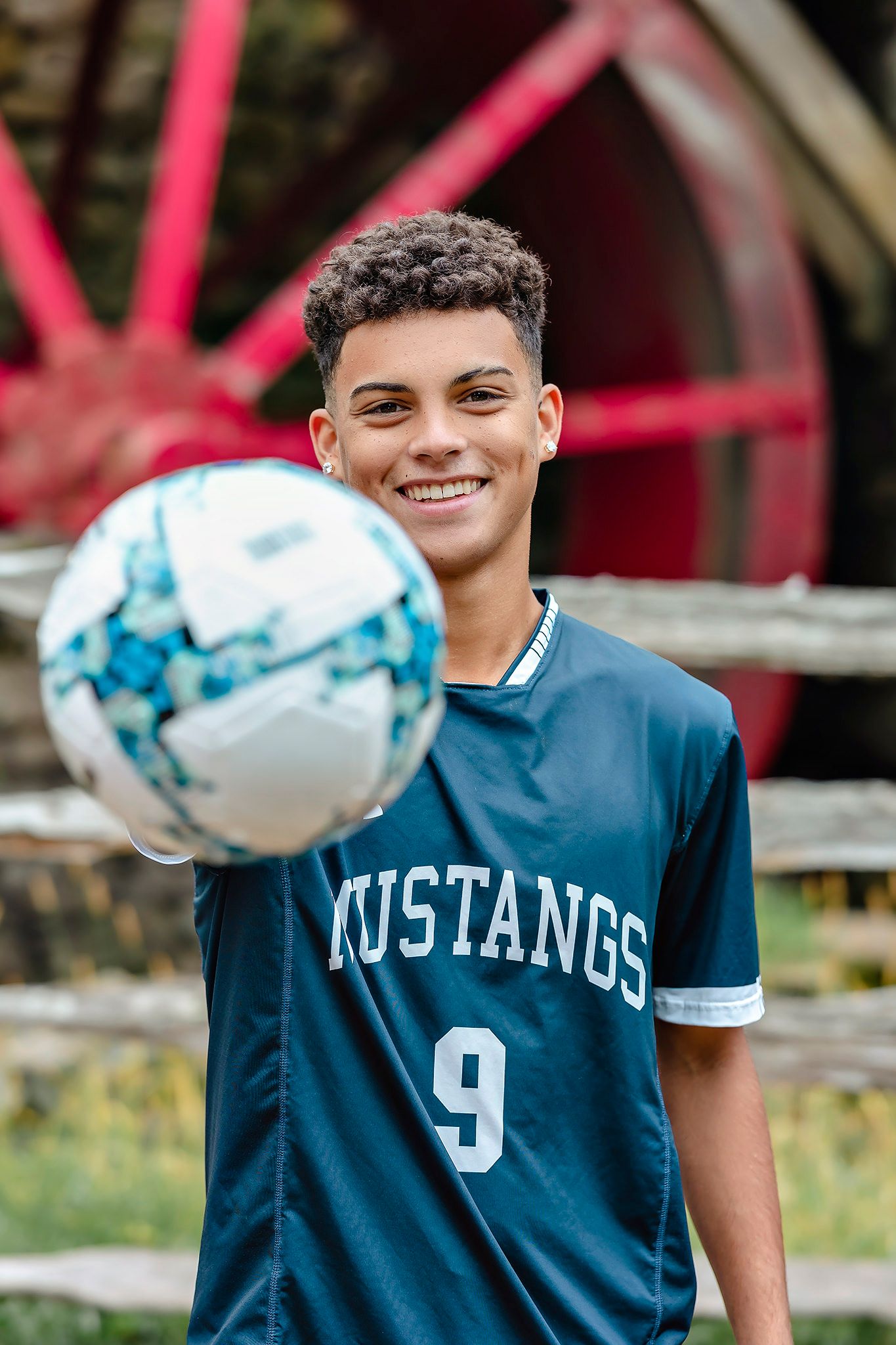 Soccer player in Mustangs jersey number 9 holding ball by historic mill.