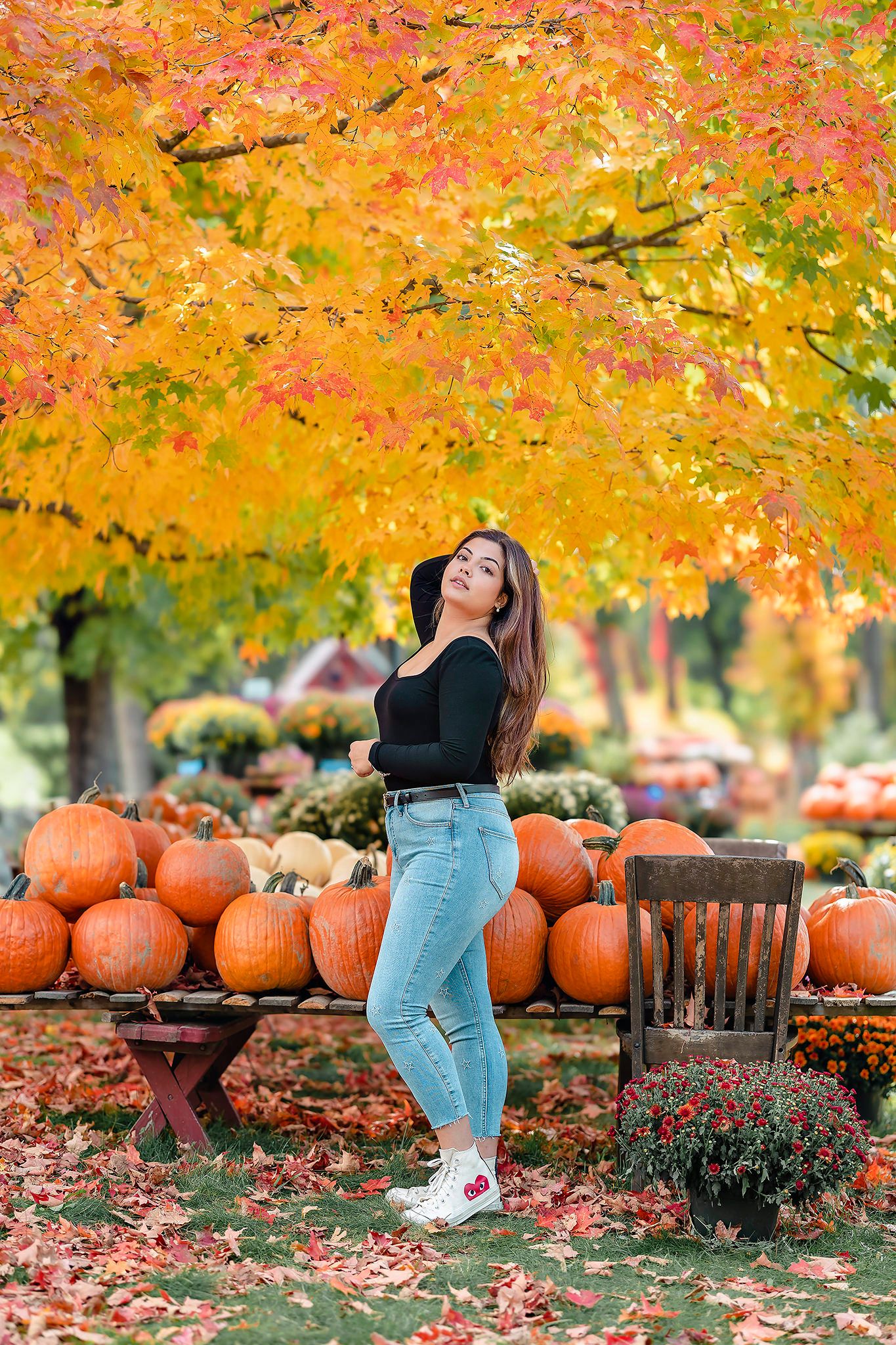 Fall scene with pumpkin display and autumn foliage featuring casual fashion against vibrant orange maple leaves.