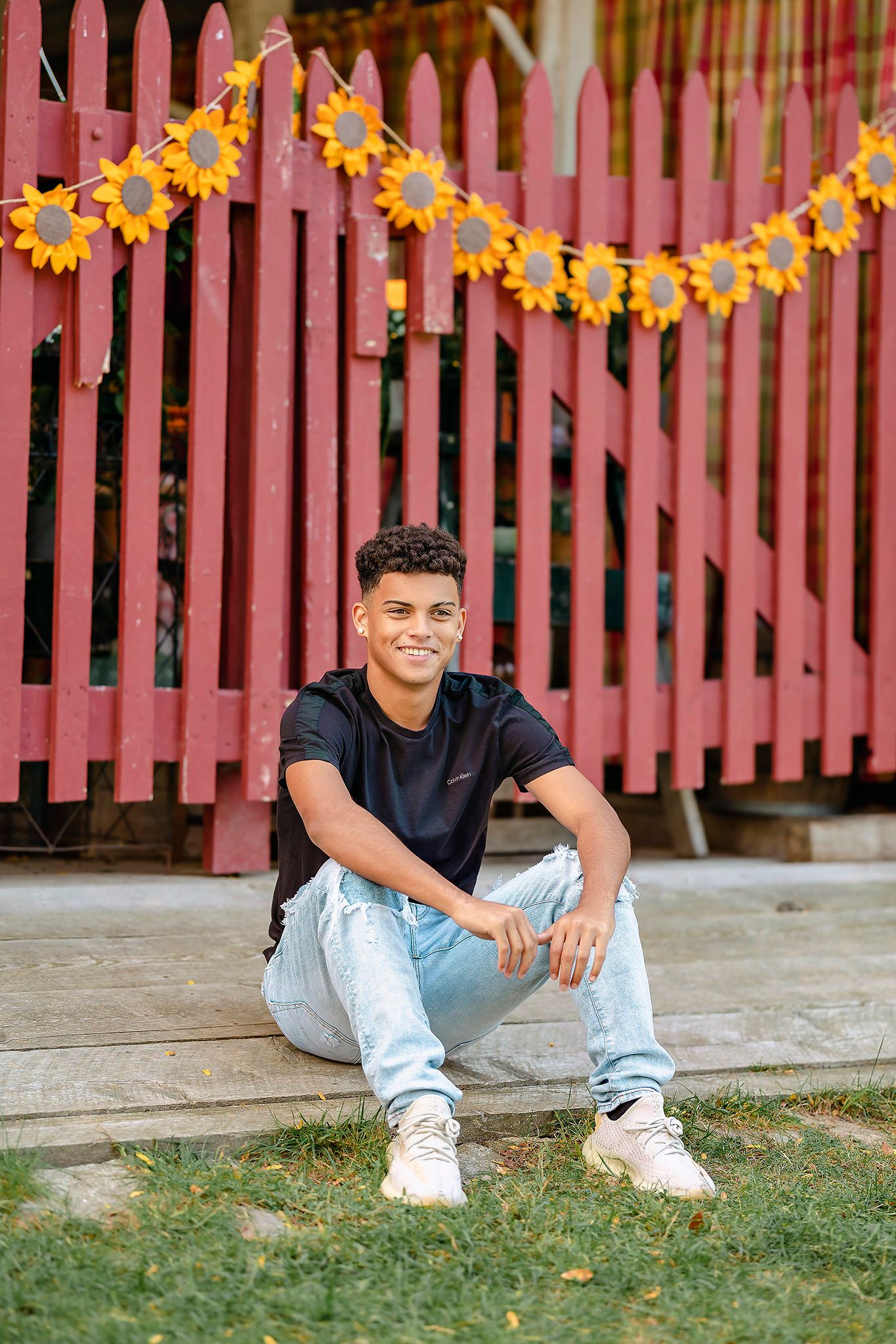 Cropped view at ground level showing feet and legs sitting near a pink fence decorated with yellow flowers.