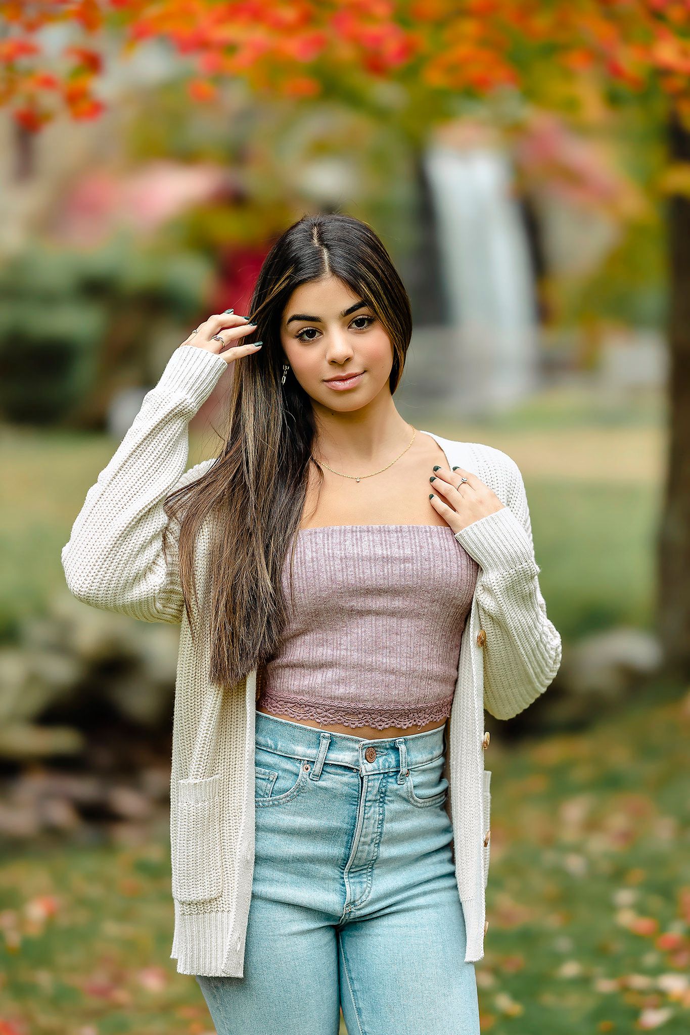 Casual autumn fashion portrait with cozy knit cardigan and jeans against fall foliage.
