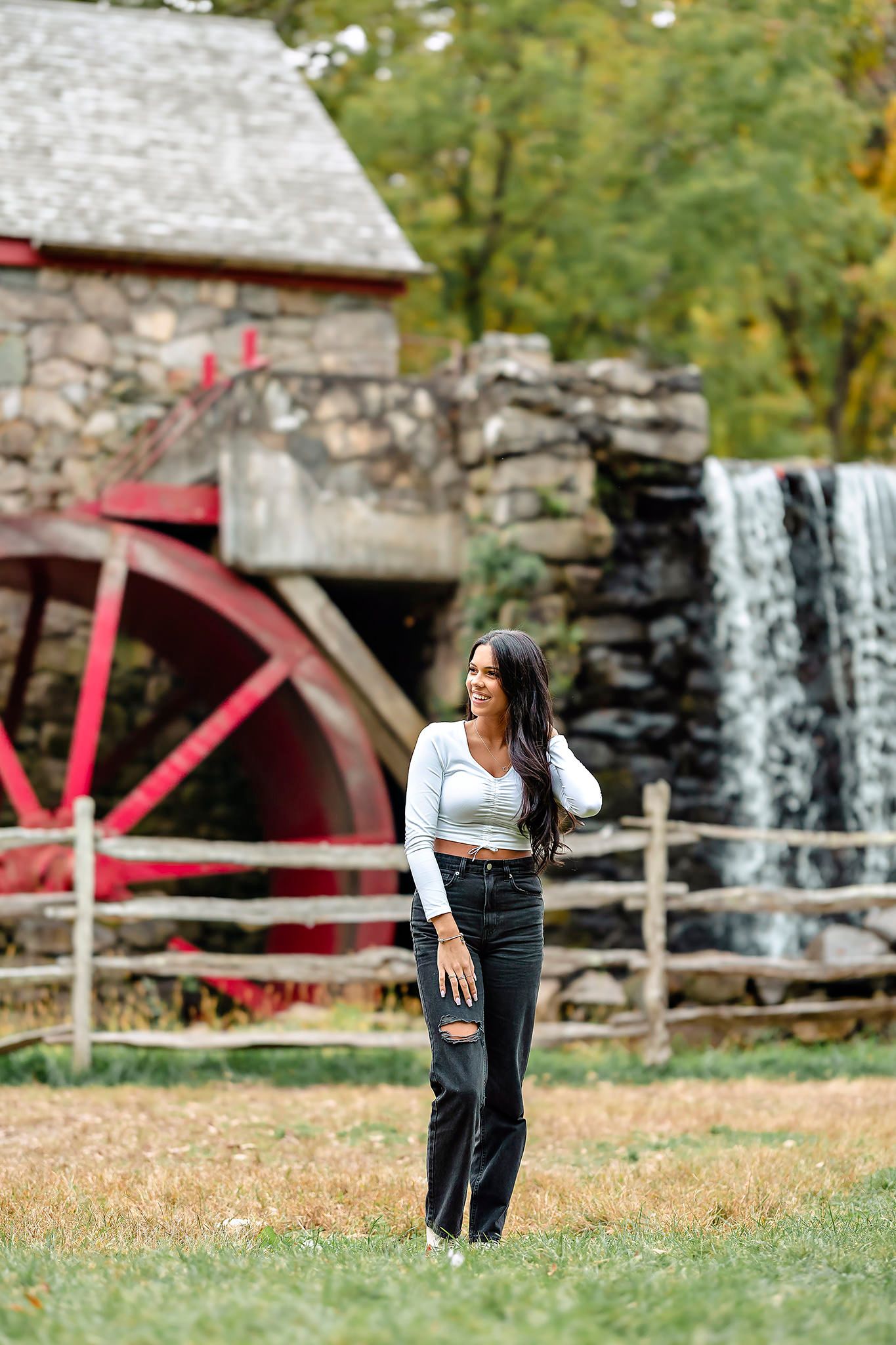Fashion portrait by historic stone water mill with red wheel in autumn setting.