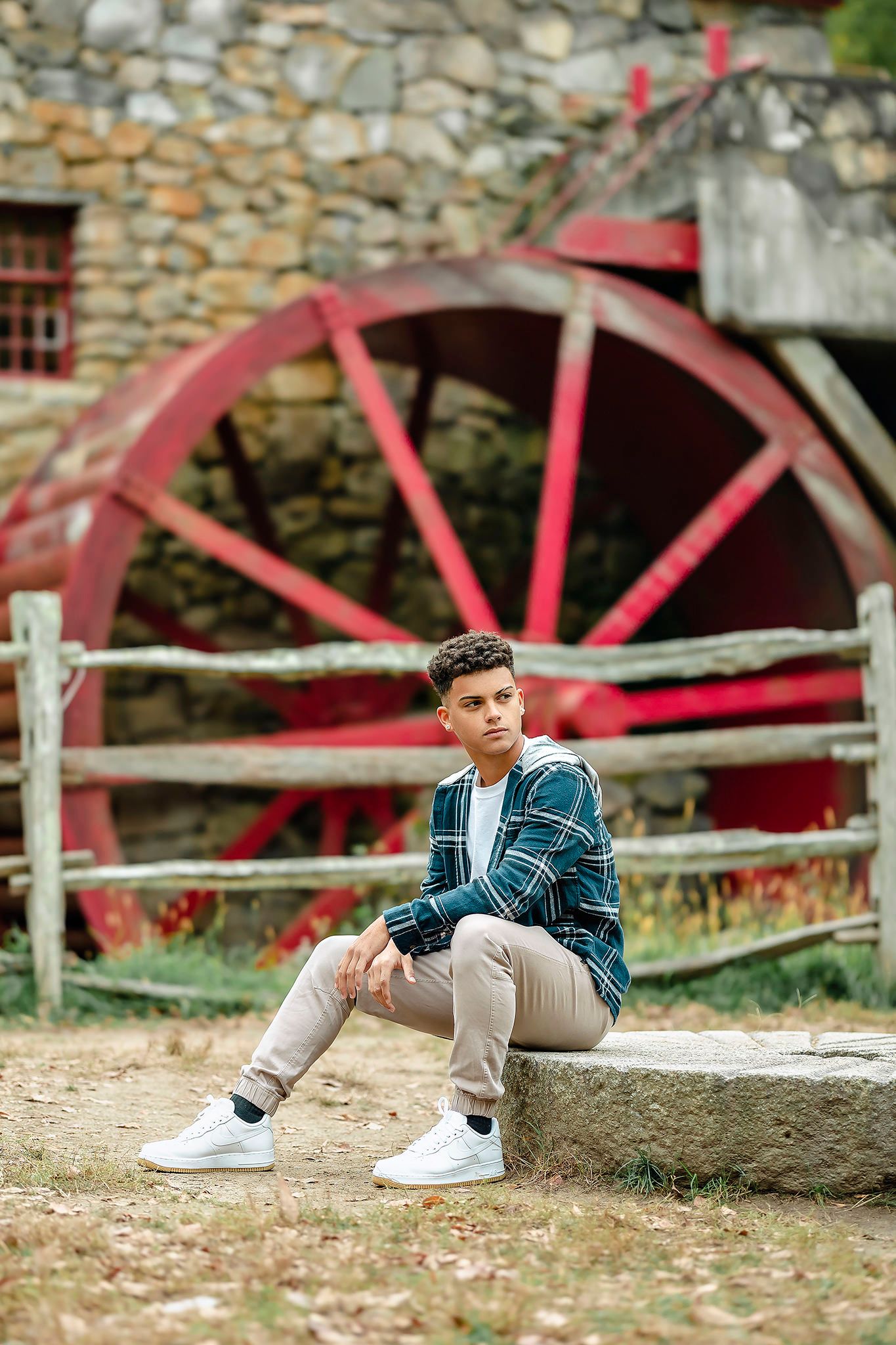 Soccer player in plaid shirt sitting by historic mill with red water wheel.