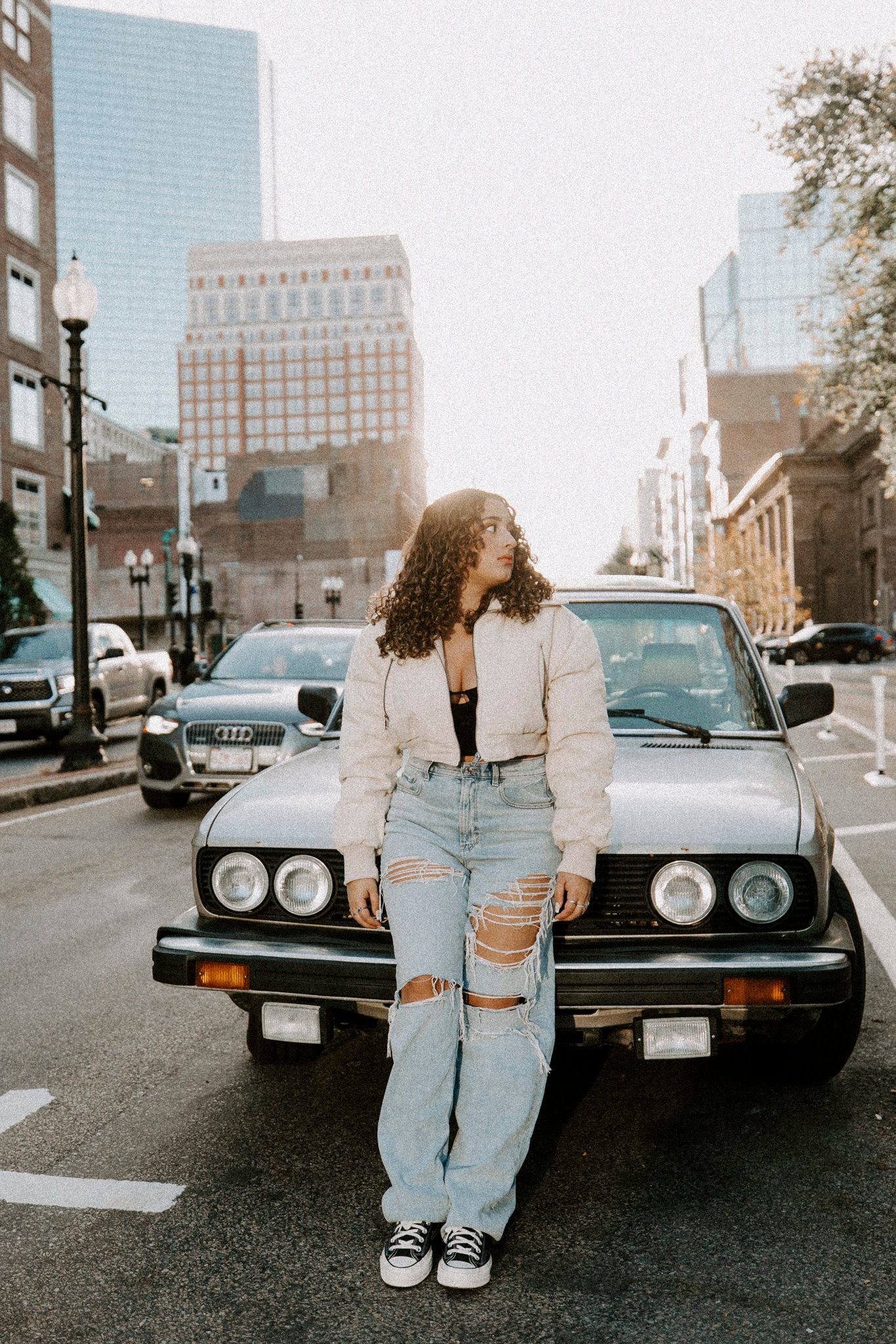 Casual street photography session featuring person in denim and white jacket with black car.