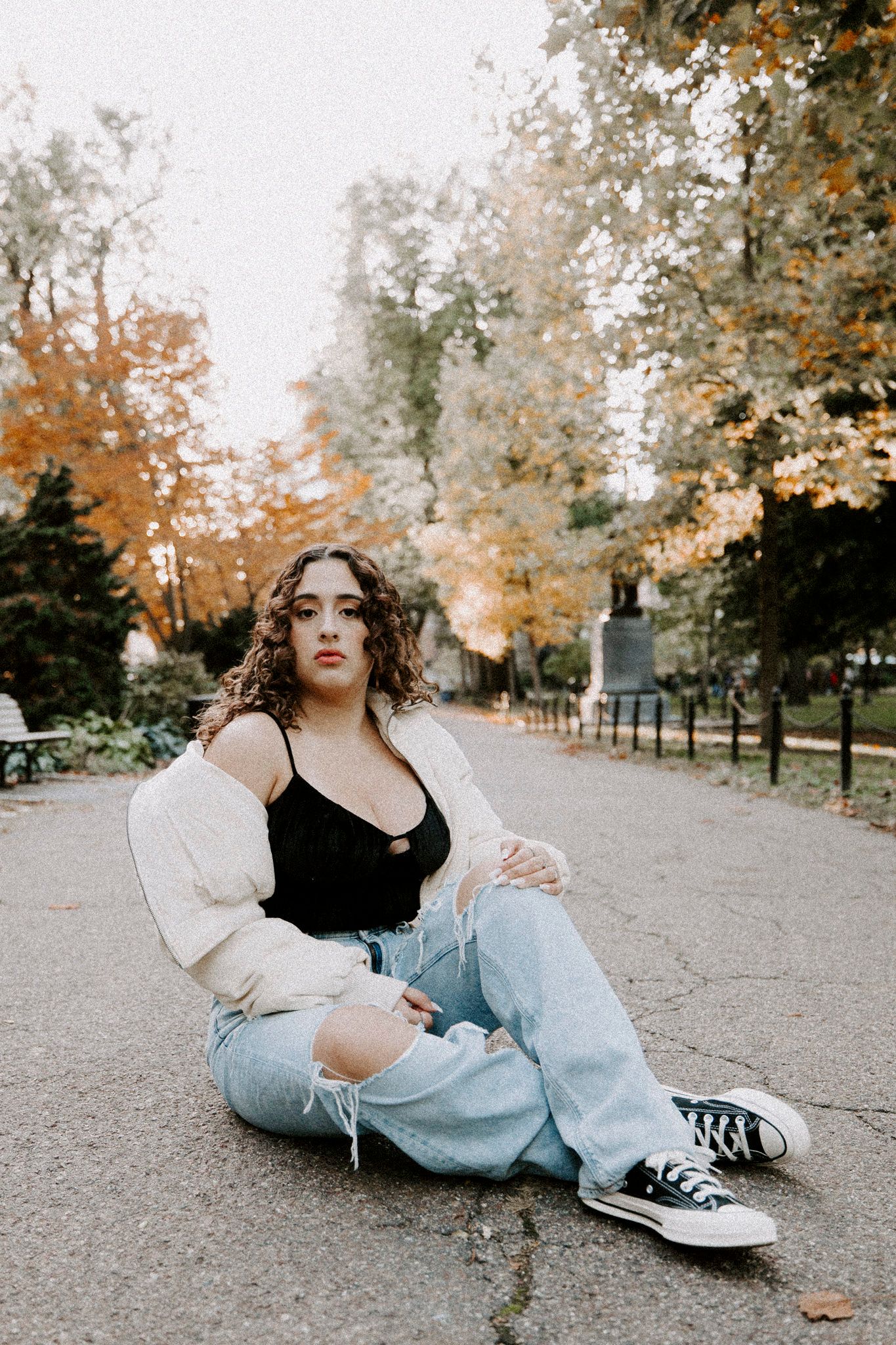 Person in casual attire relaxes on ground with autumn foliage in background.