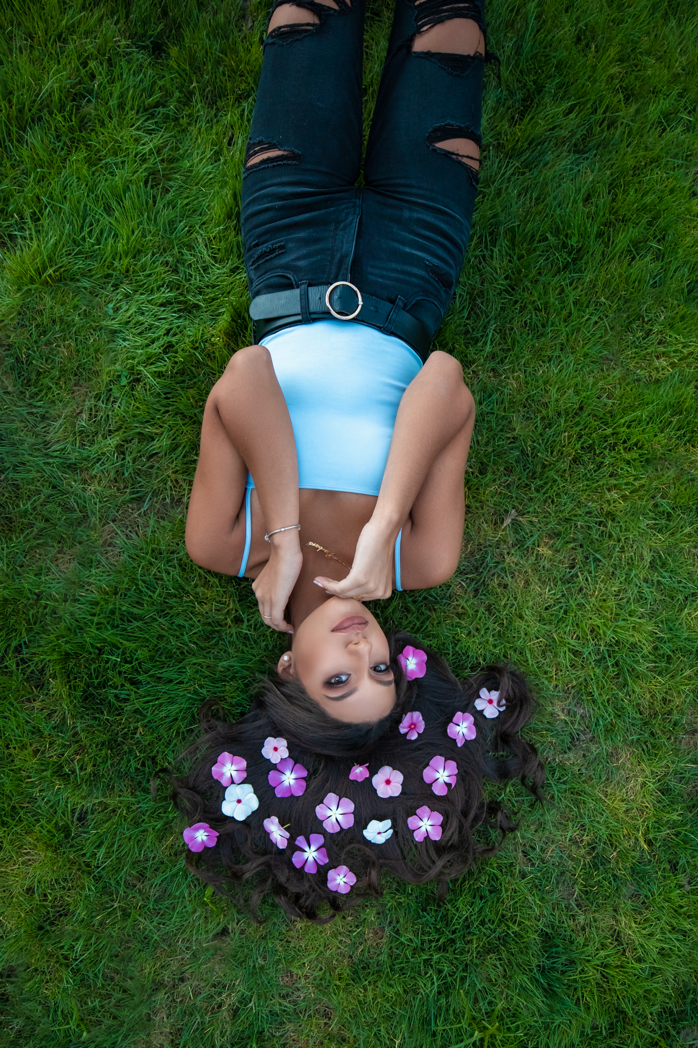 Creative portrait on grass with scattered purple flowers creating whimsical effect.
