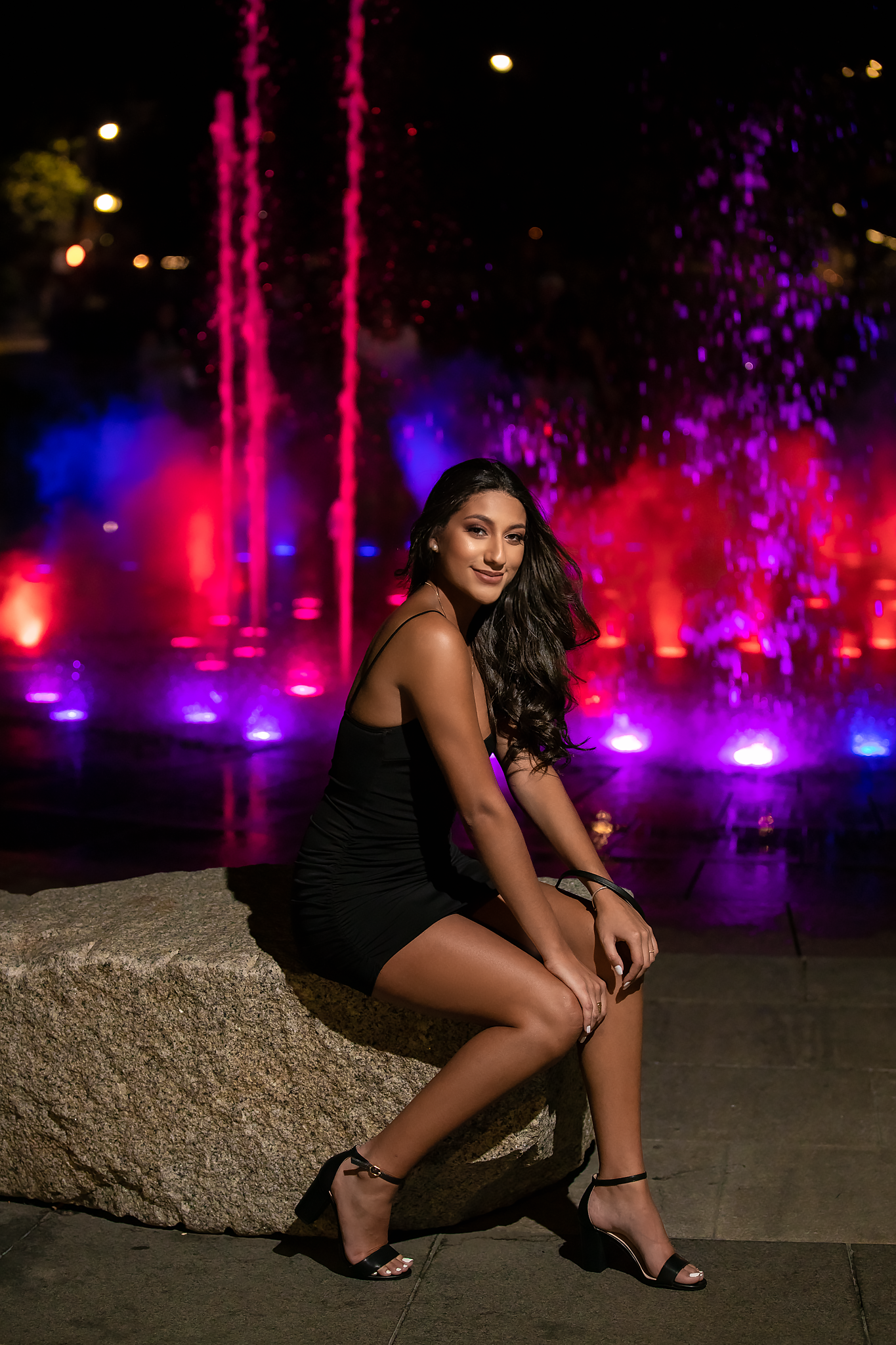 Illuminated fountain display with purple and red lights creating dreamy nighttime scene.