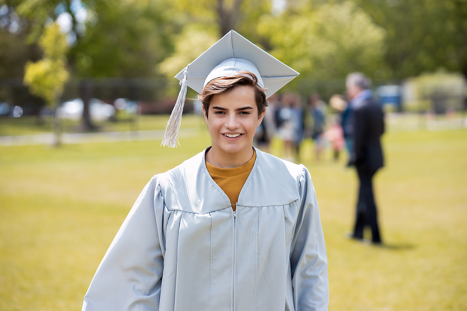 Happy graduate in cap and gown smiles on green university campus.