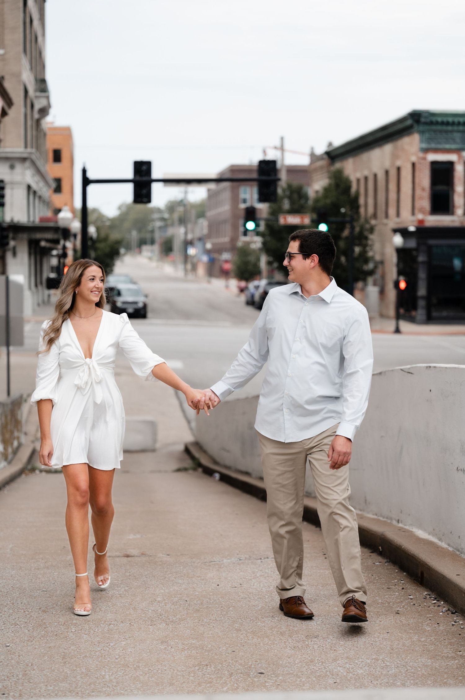 A couple in white outfits holds hands while walking down a city street.