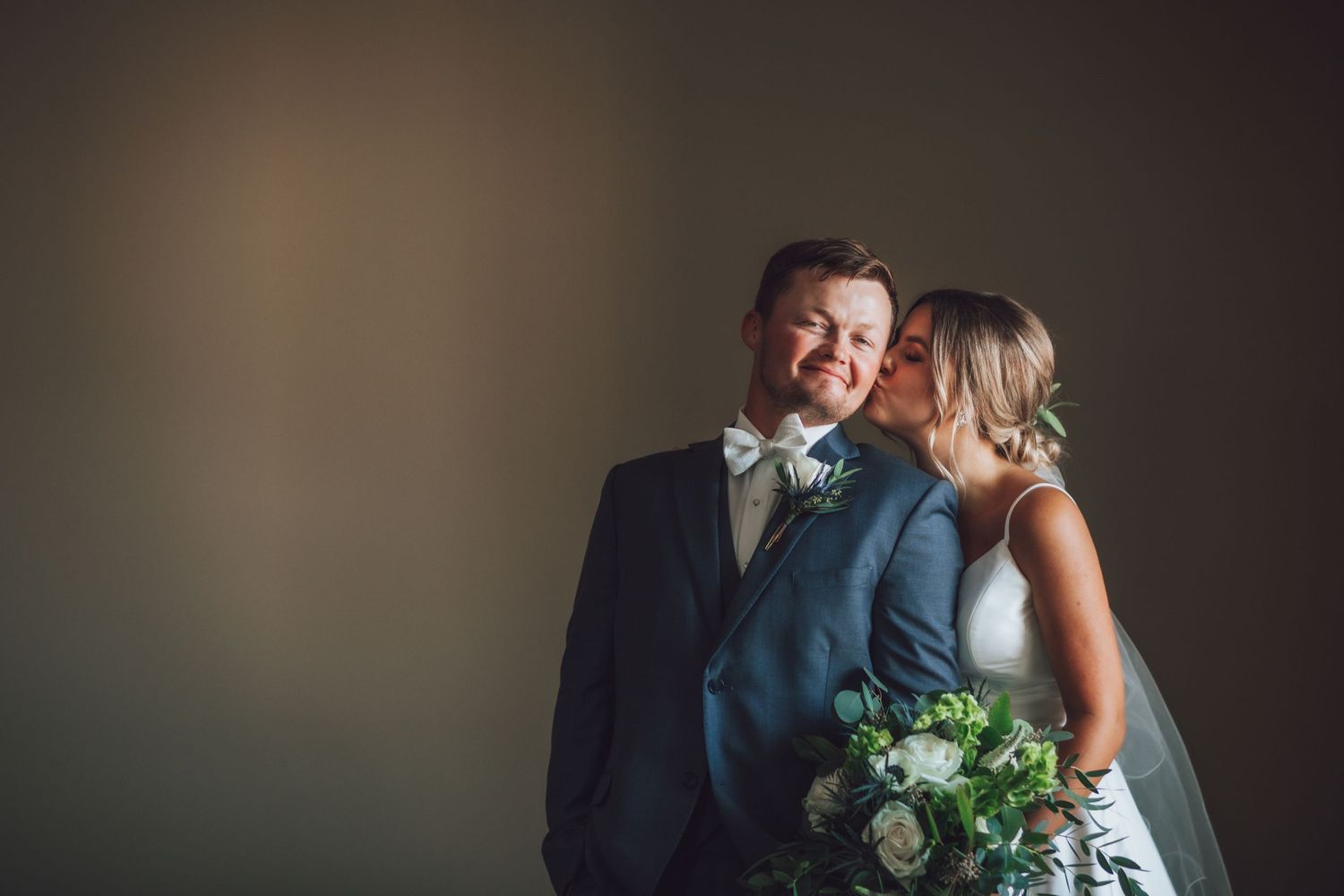 A romantic wedding portrait showing a couple embracing in dramatic lighting against a dark background.